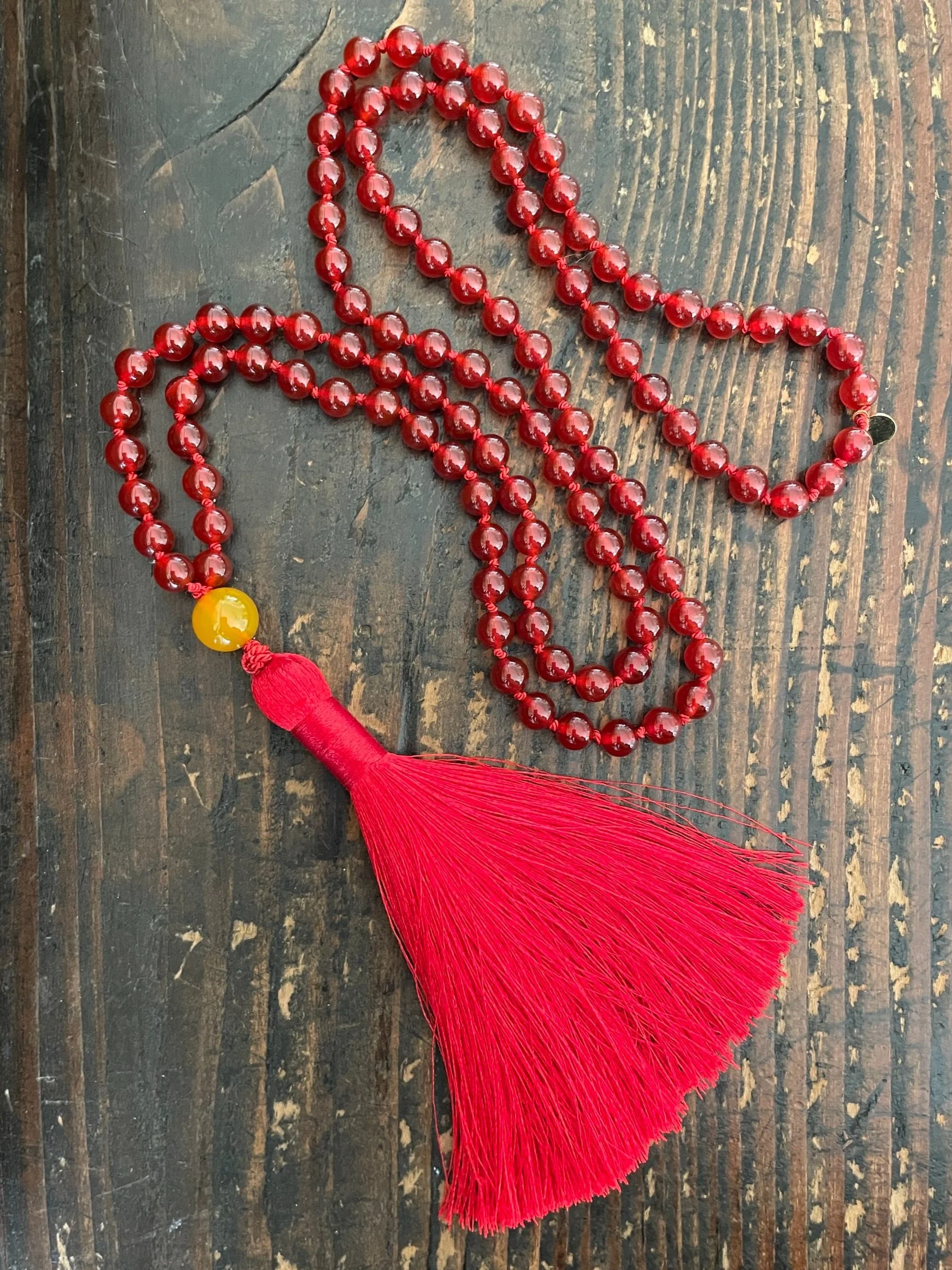 Red Carnelian meditation prayer beads with a large red tassel resting on a dark wooden surface.