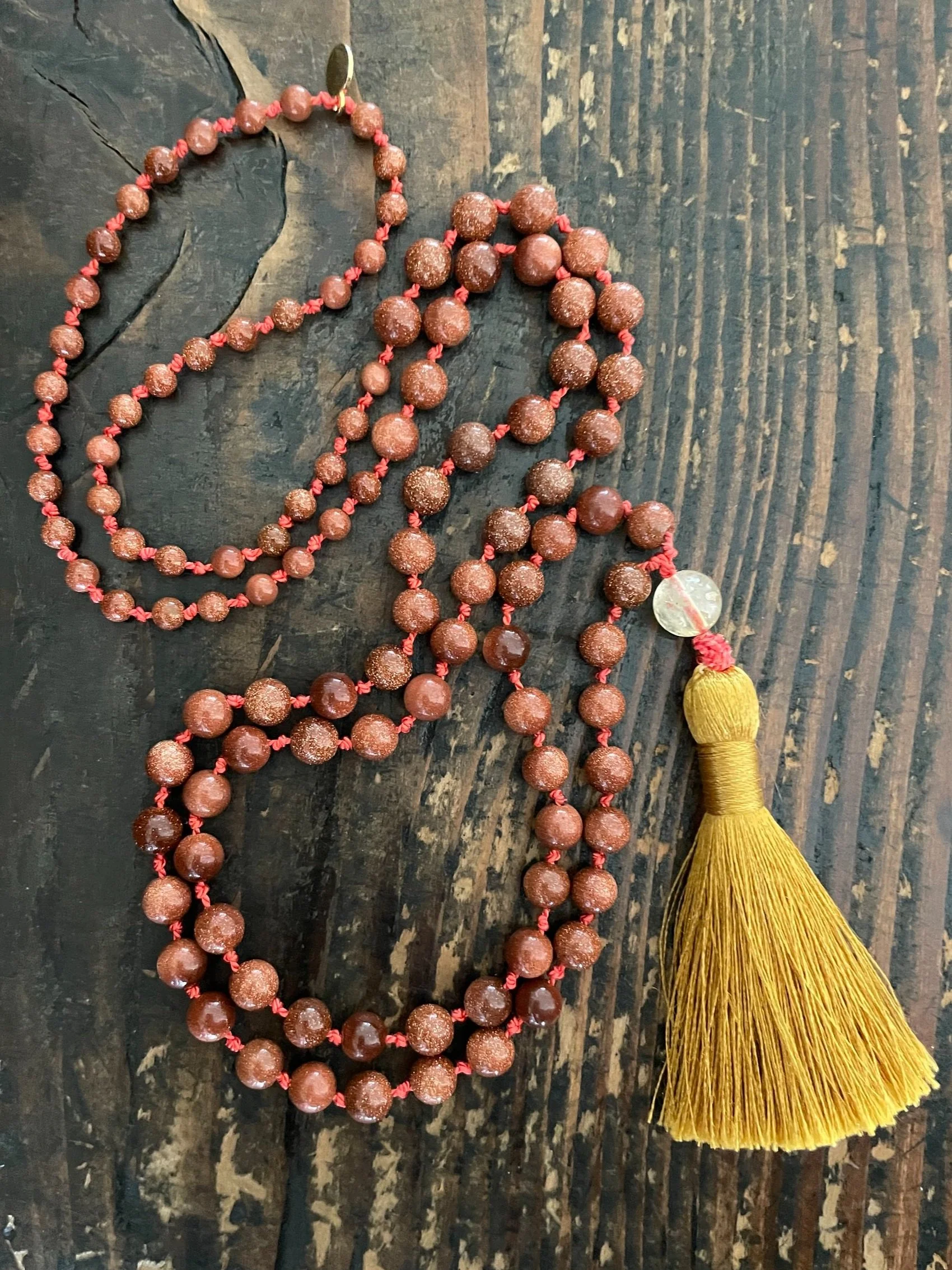 A string of gold stone beads with a yellow tassel on a dark wooden surface.