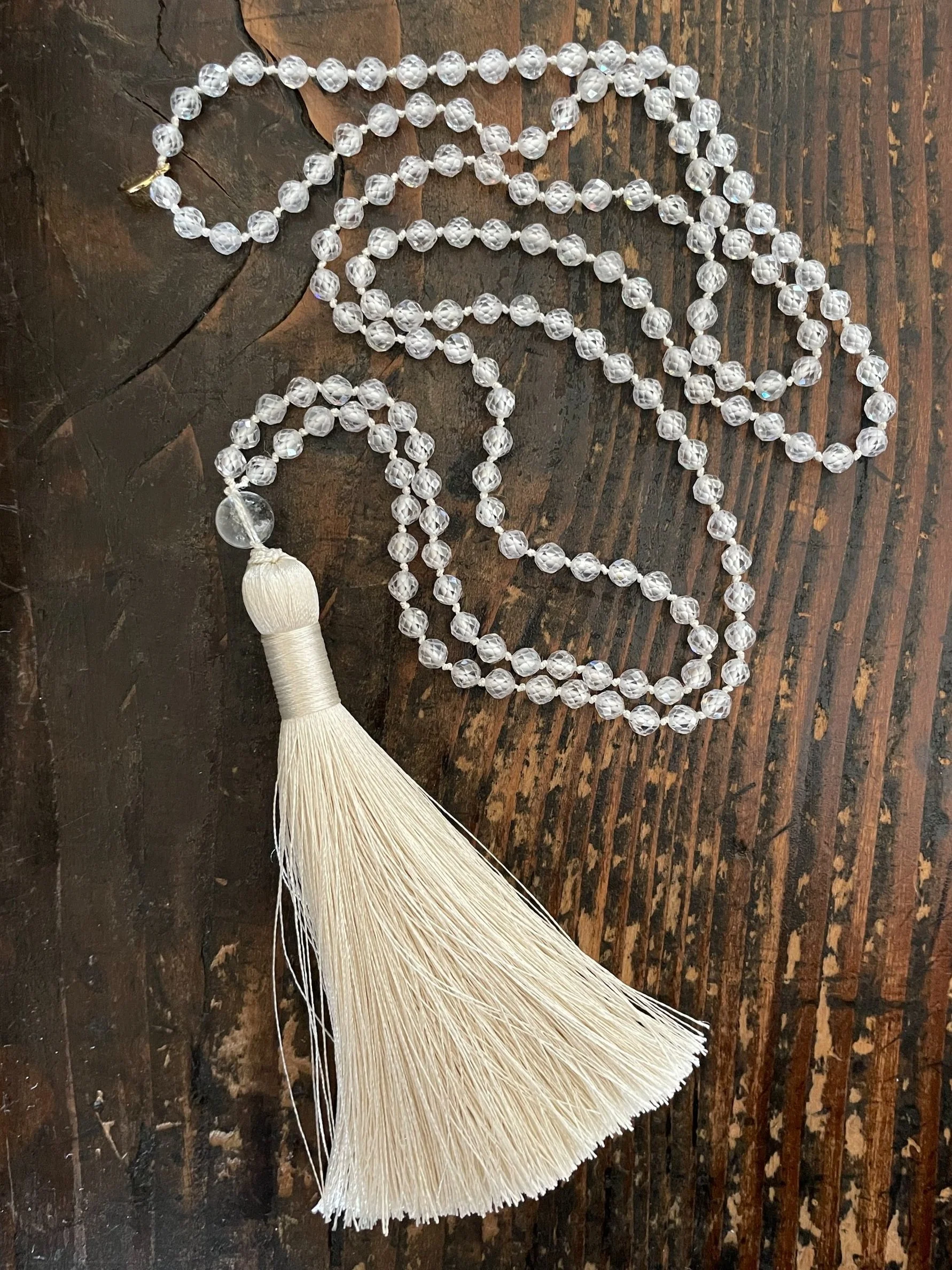 String of zircon beads with a white tassel at one end, laid out on a wooden surface.