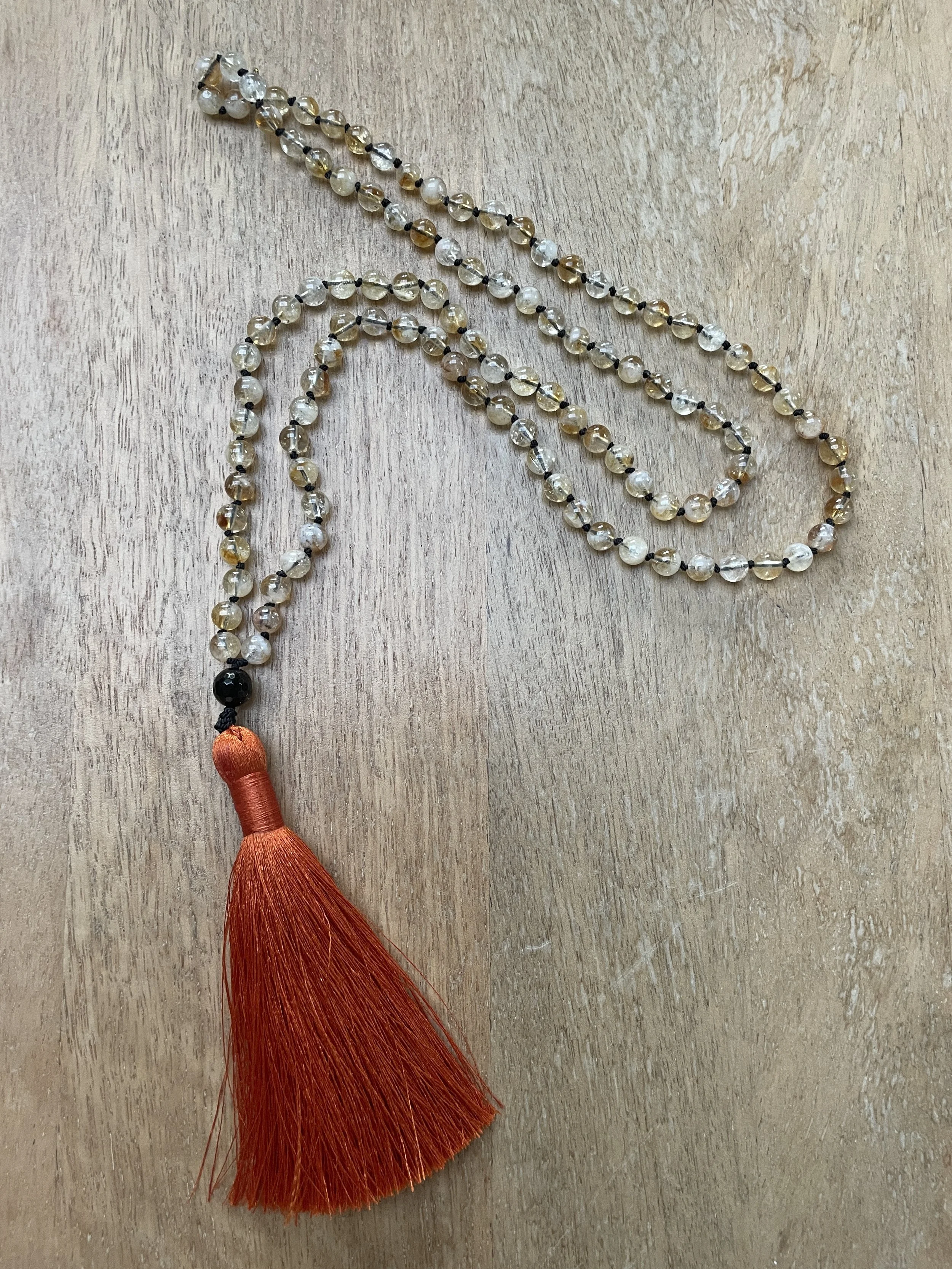 Beaded necklace with citrine beads, a black onyx beads, and a red tassel pendant, laid on a wooden surface.