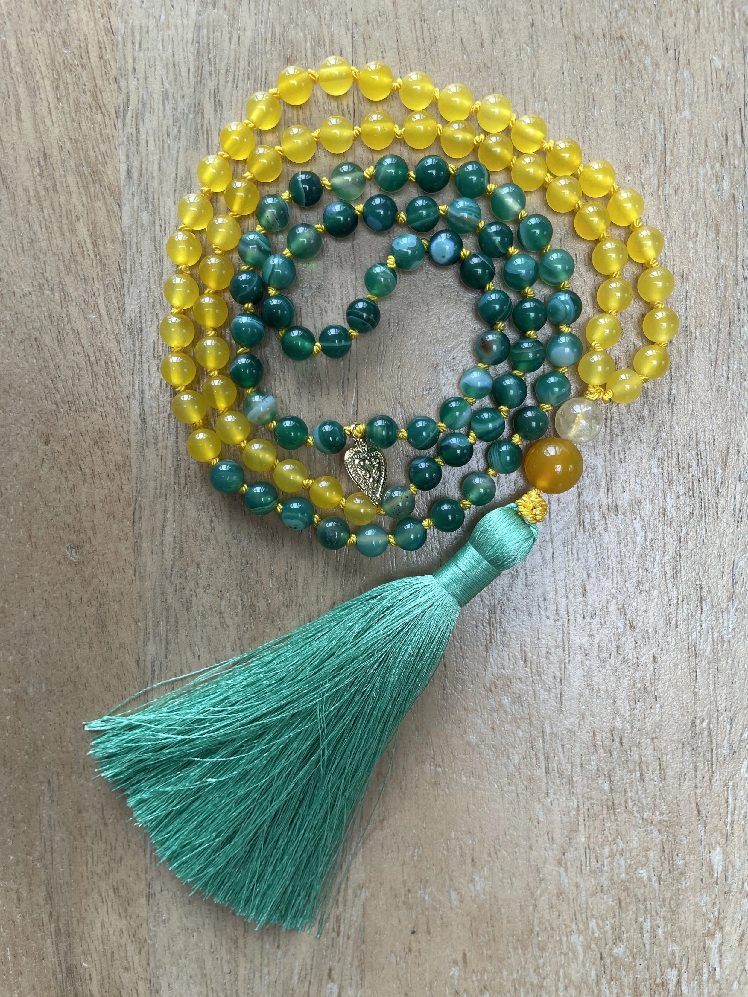 Green & yellow agate, a heart-shaped pendant, and a large turquoise tassel, laid on a wooden surface.