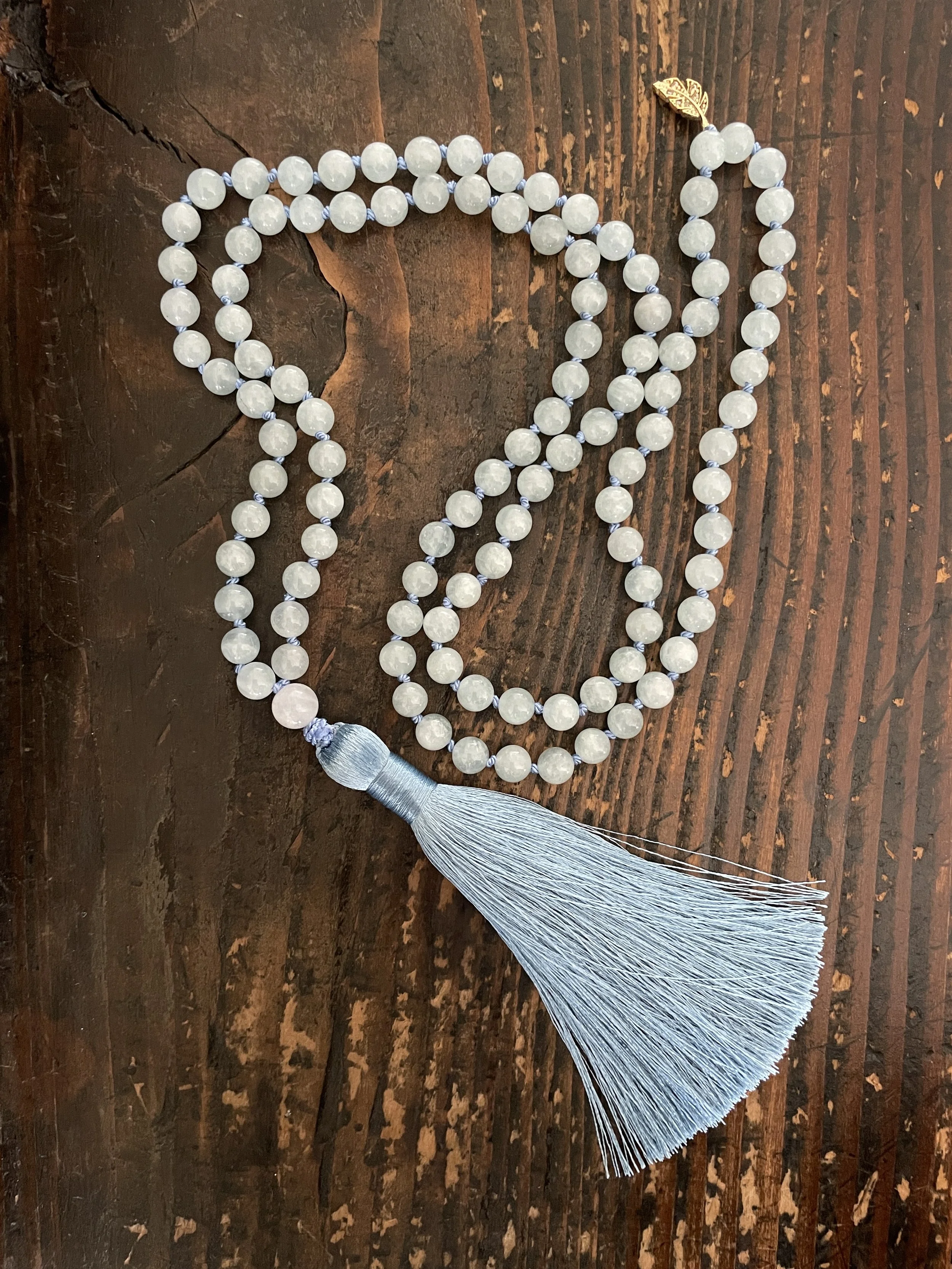 Beaded prayer necklace with a silver tassel on a wooden surface.
