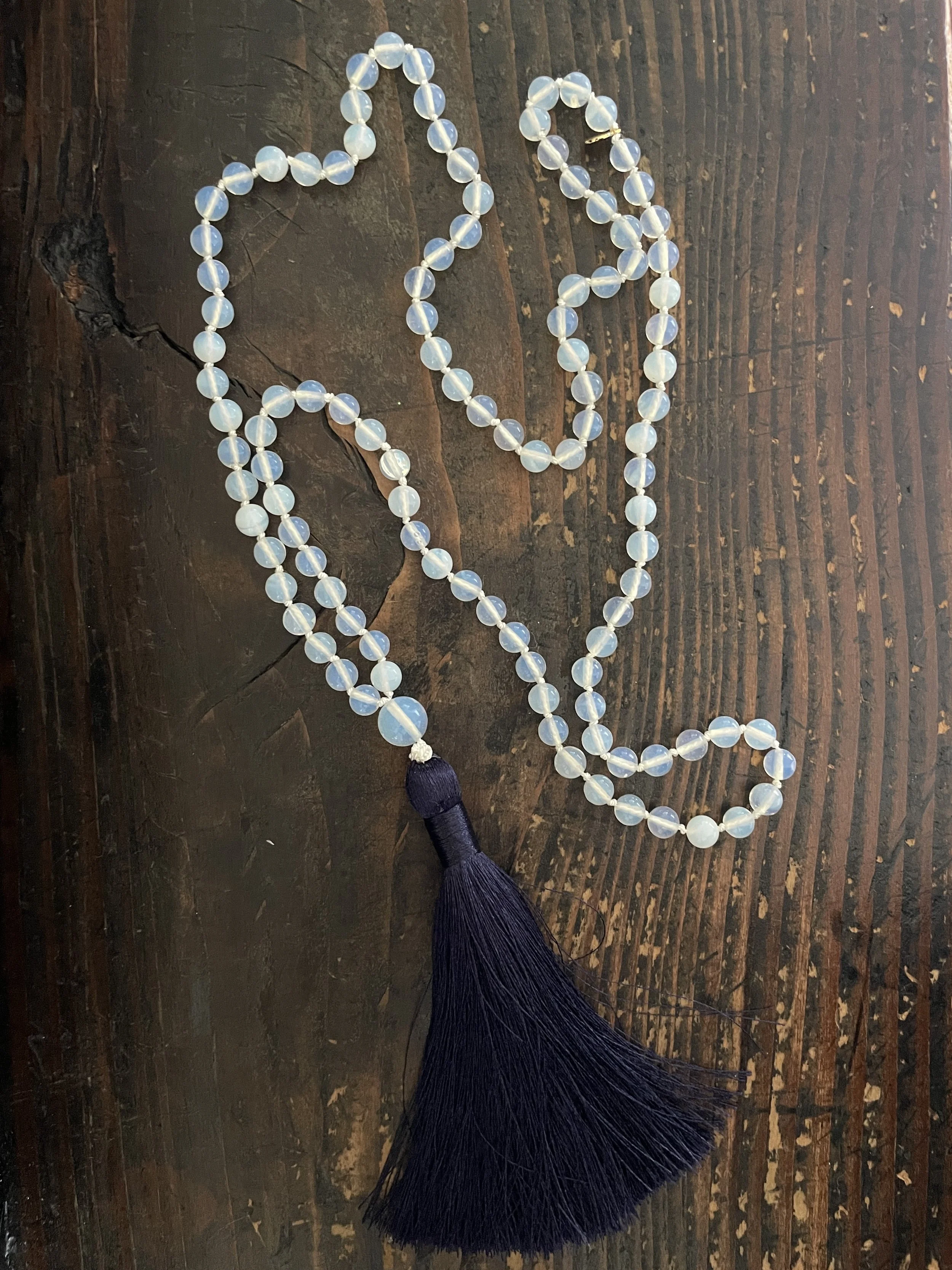 Moonstone mala necklace with a dark purple tassel on a wooden surface.