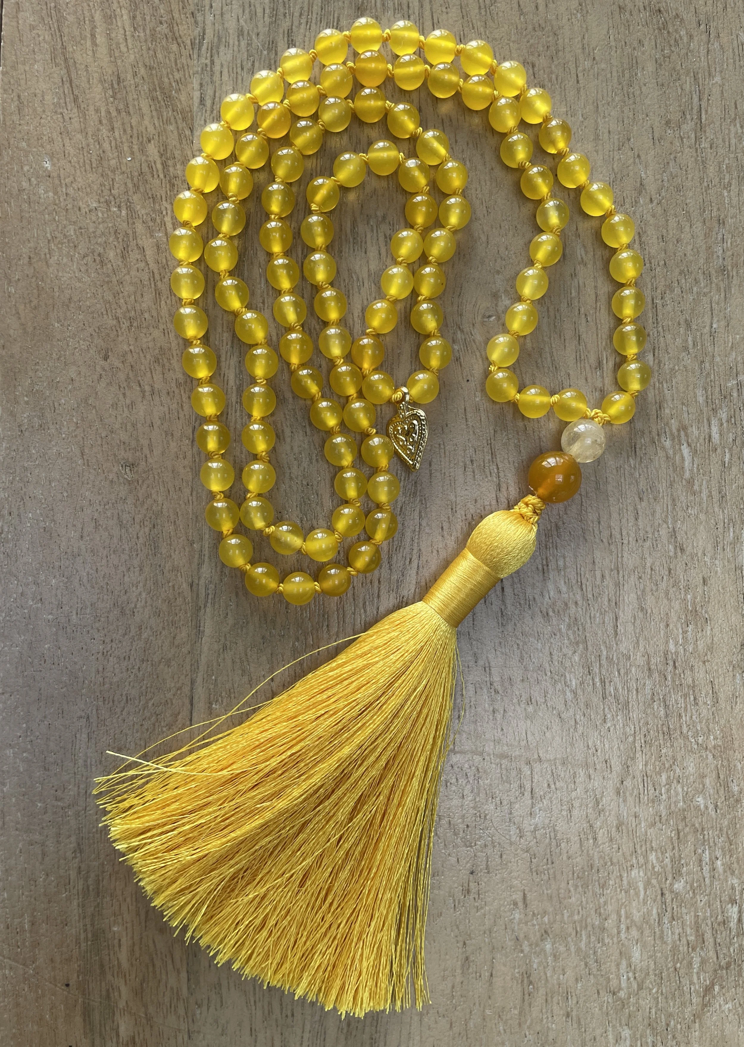 Yellow Agate beads with a large yellow tassel and a small gold charm, arranged on a wooden surface.