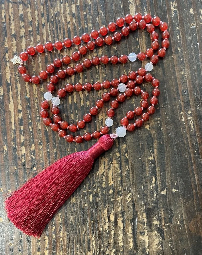 Red Carnelian beaded mala necklace with a red tassel, resting on a wooden surface.