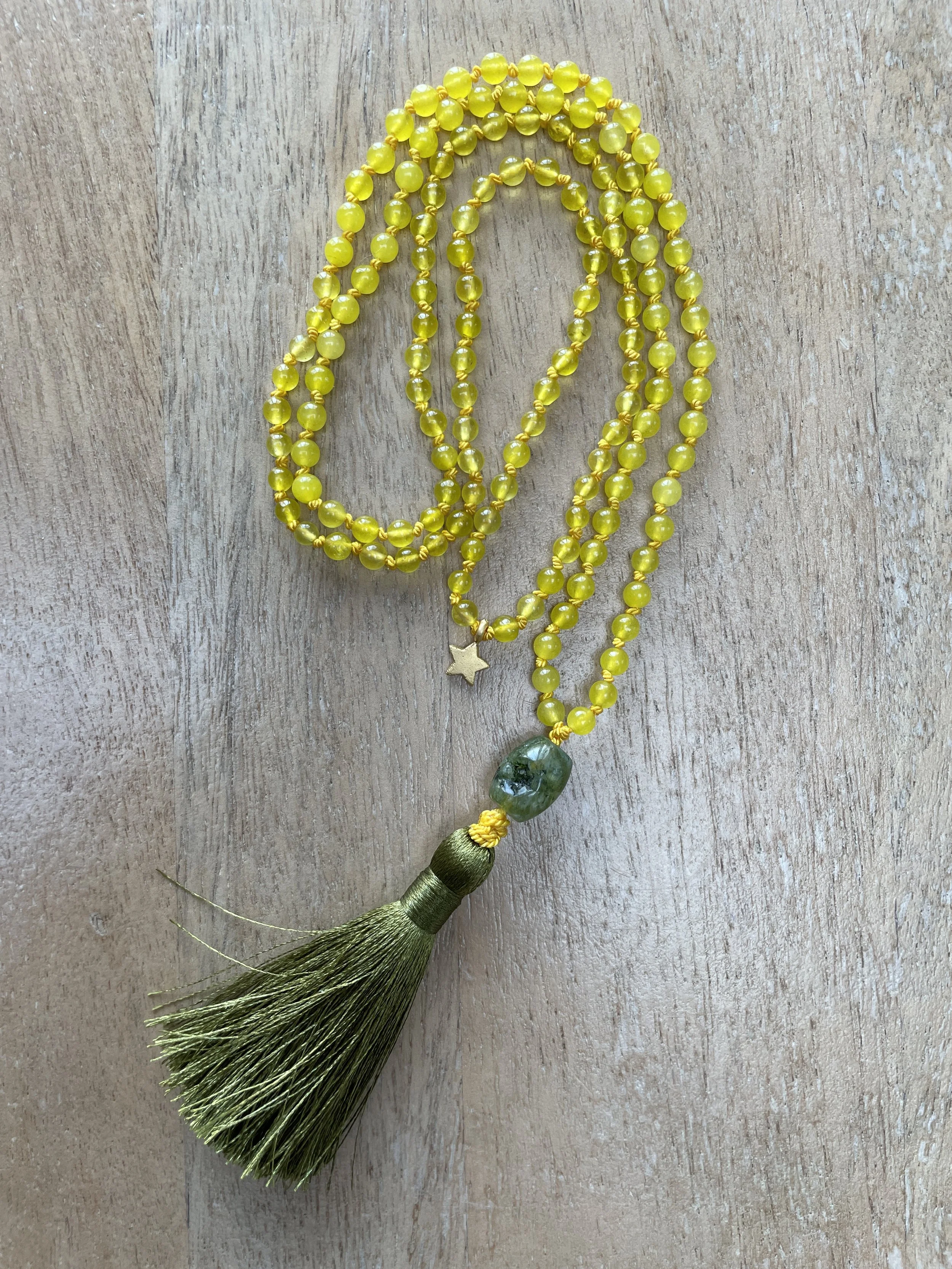 Yellow agate necklace with a green moss agate bead, gold tassel, and star-shaped pendant on a wooden surface.