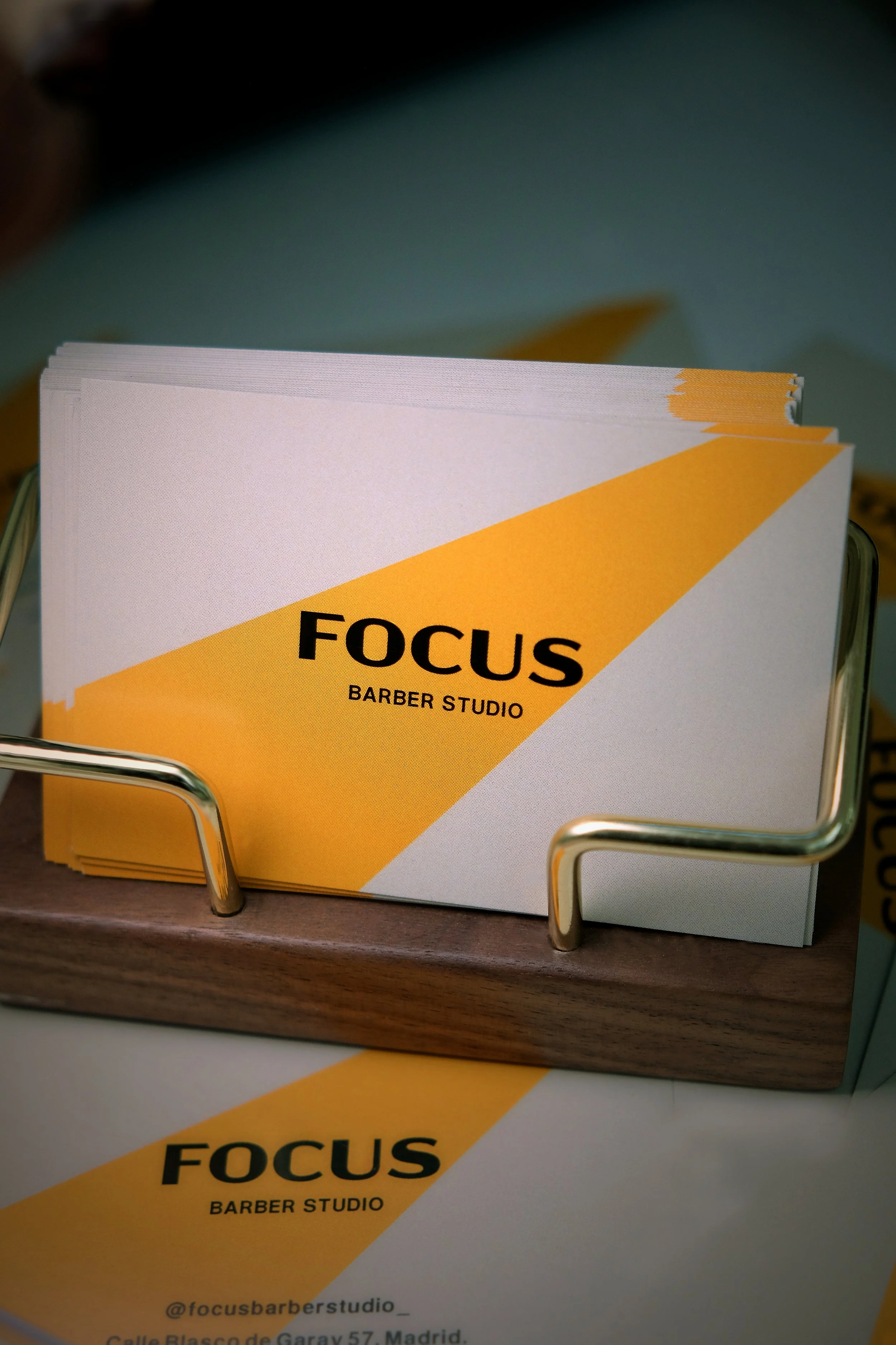 Flyers for Focus Barber Studio with yellow and white design, placed in a metal holder on a wooden surface.