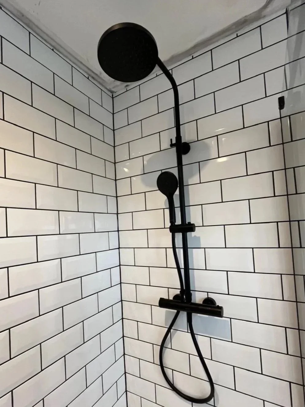 A black wall clock showing 2:55, mounted on a plain light-colored wall, and a black radiator with exposed pipes at the bottom of the wall, with a dark wooden floor.