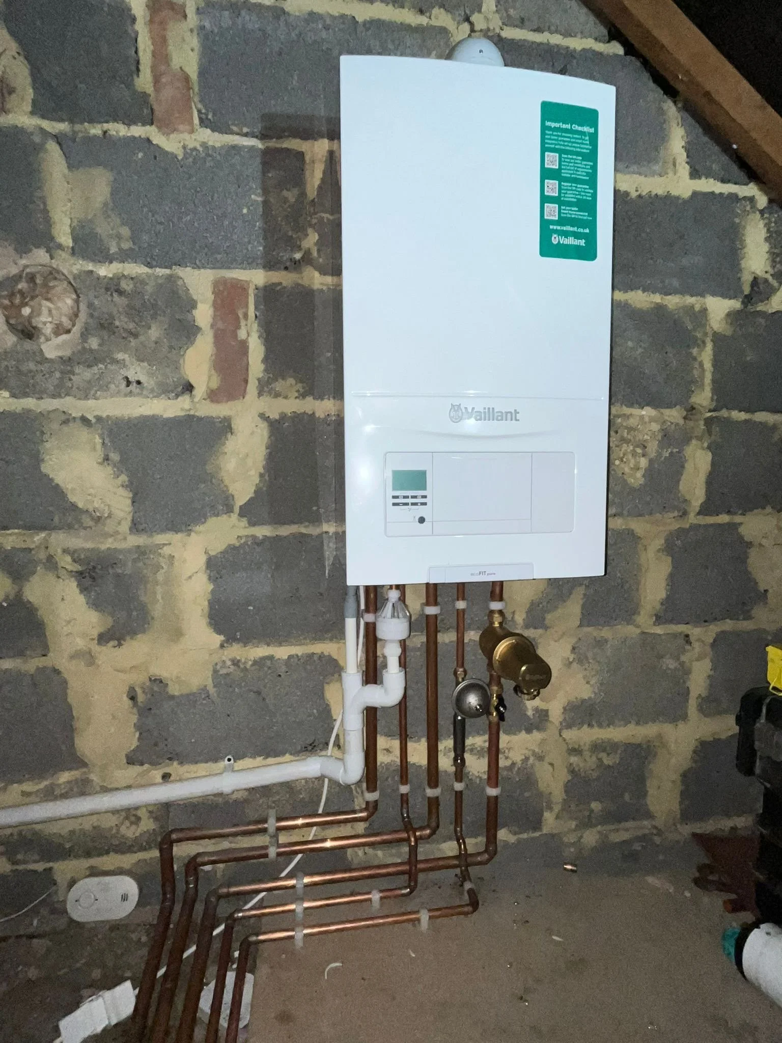 A white Worcester boiler installed on a gray brick wall in an attic or unfinished space, with digital display, control dials, and pipes connected underneath.
