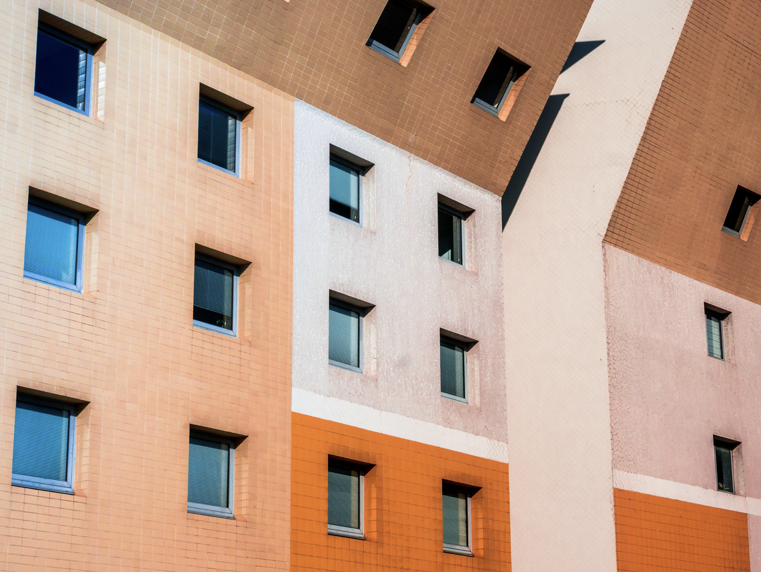 Façade d'un bâtiment moderne en briques avec des fenêtres carrées et des teintes de beige, blanc et orange.