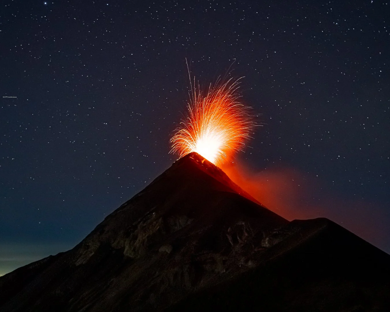 Éruption nocturne d'un volcan avec des projections de lave.