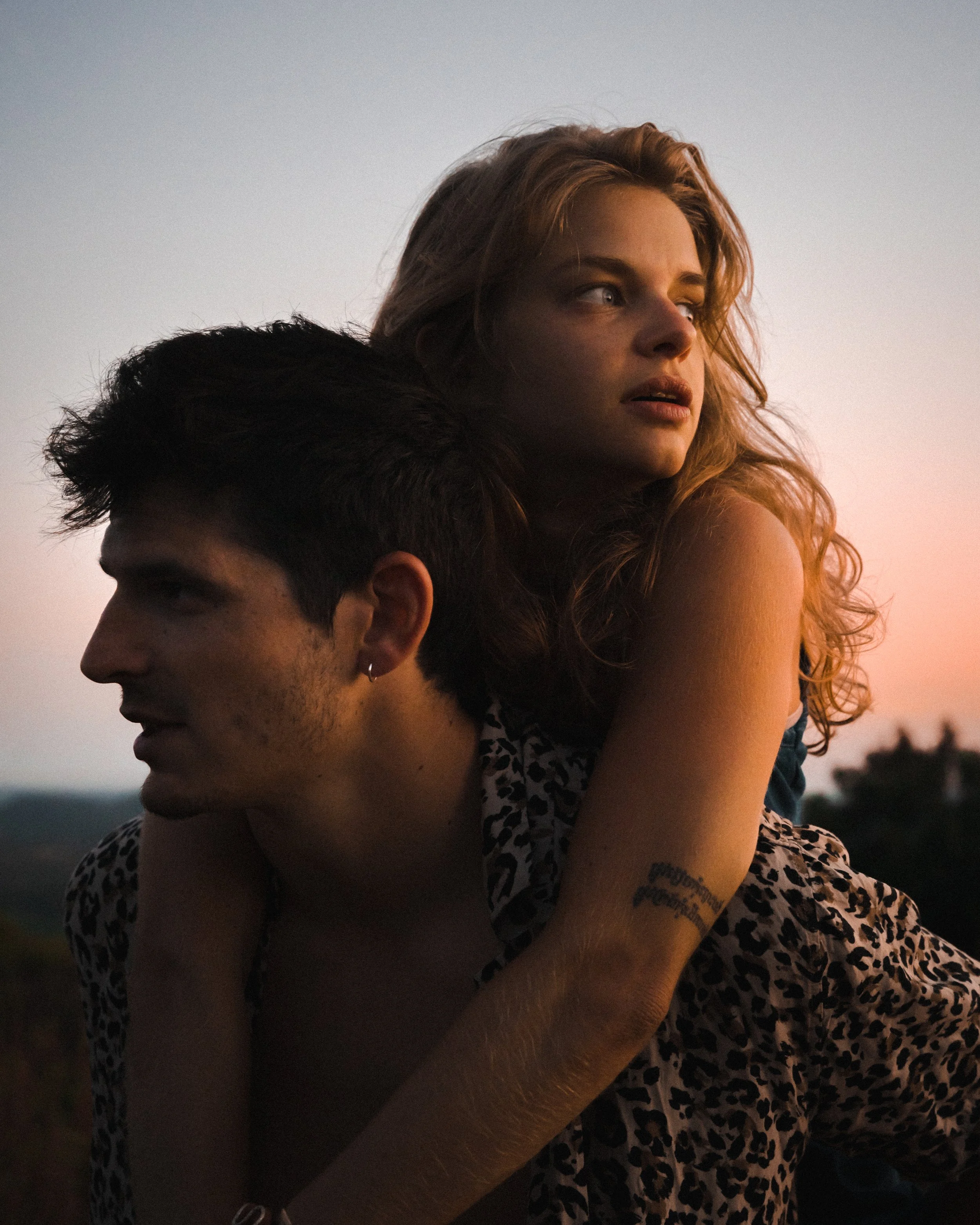 Un homme portant une chemise à imprimé léopard donne un tour de dos à une femme blonde au coucher du soleil.