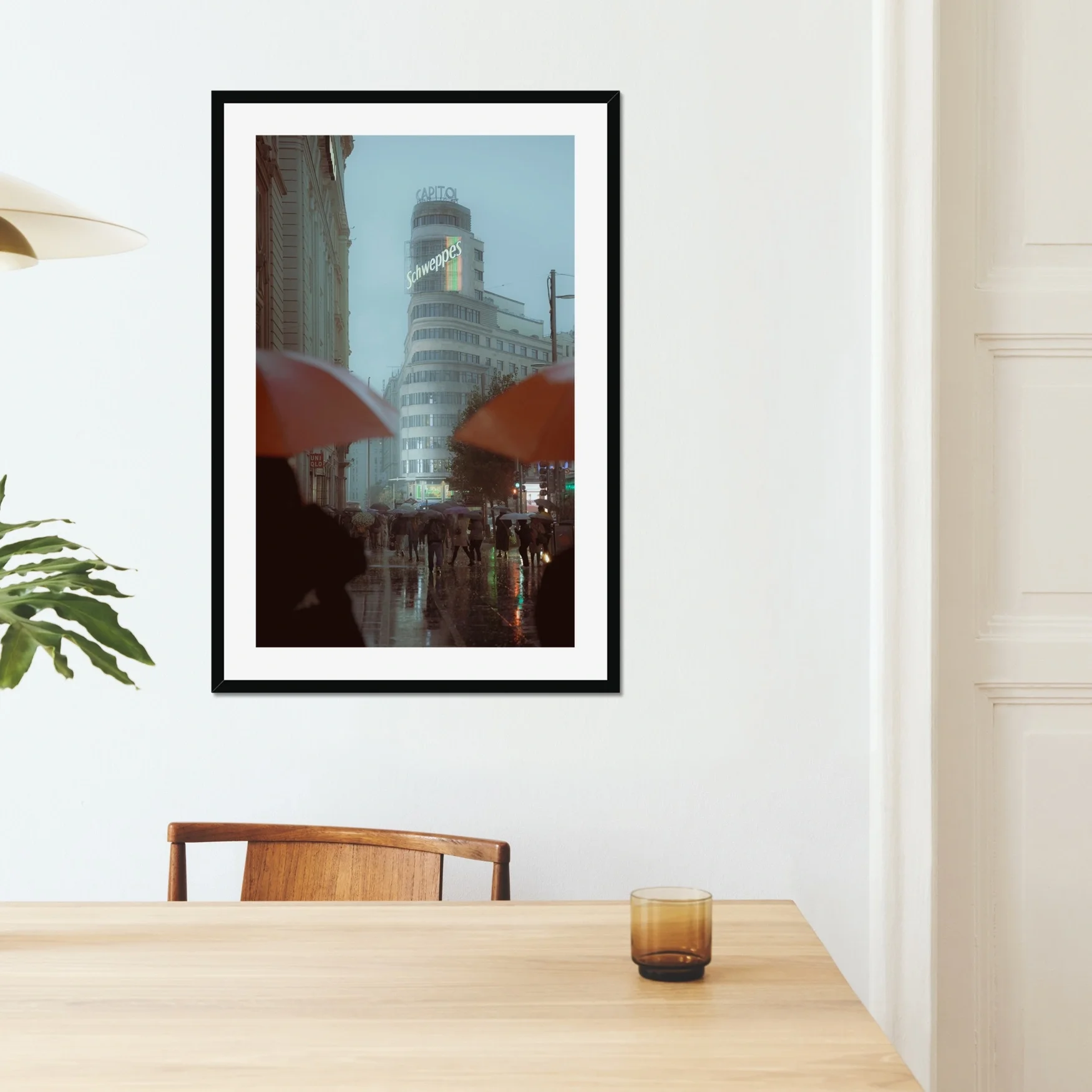 Cinematic street photography of Gran Via Madrid in the rain, featuring the Schweppes Capitol building, a sea of umbrellas, and wet street reflections at dusk.