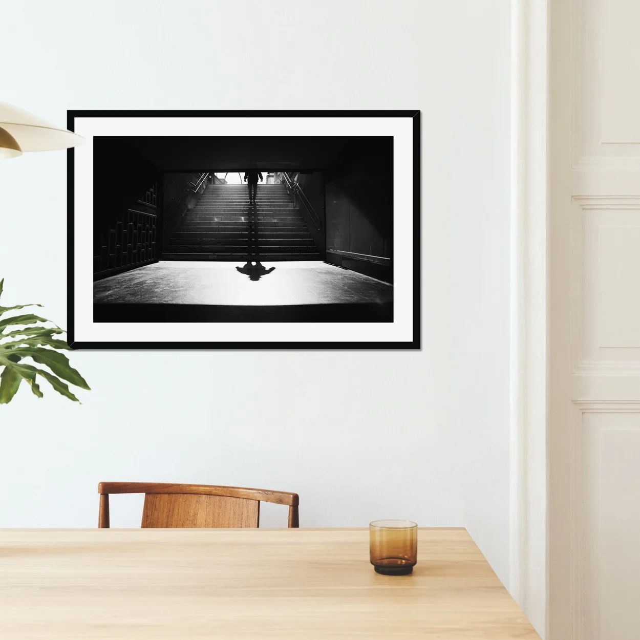 Black and white minimalist street photography of a person walking down stairs in Madrid Metro, casting a long diagonal shadow on a sunny morning.