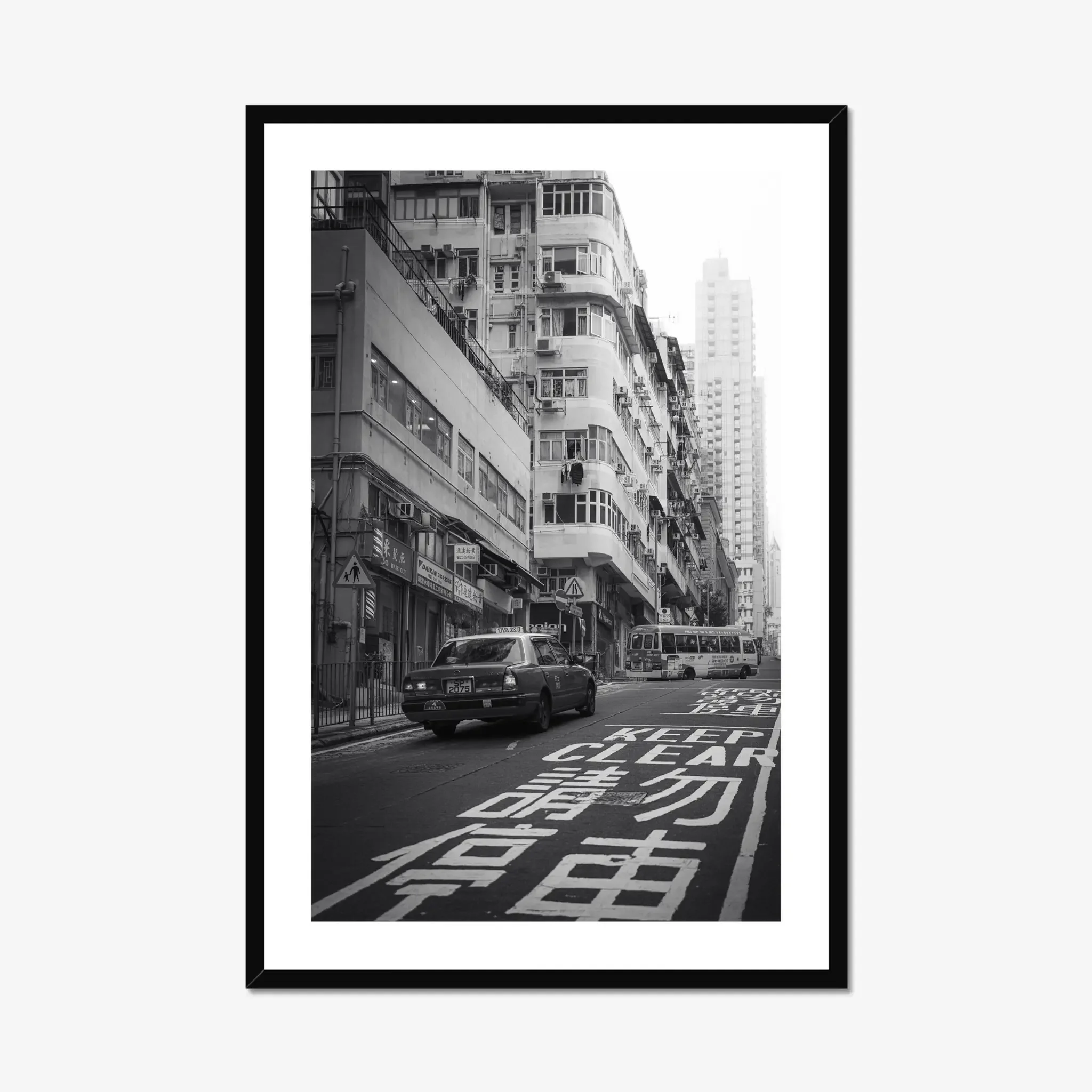 Black and white street photography print of a classic Hong Kong taxi driving up a steep hill towards a minibus. Features high-contrast shadows and strong urban geometry. Fine art wall decor