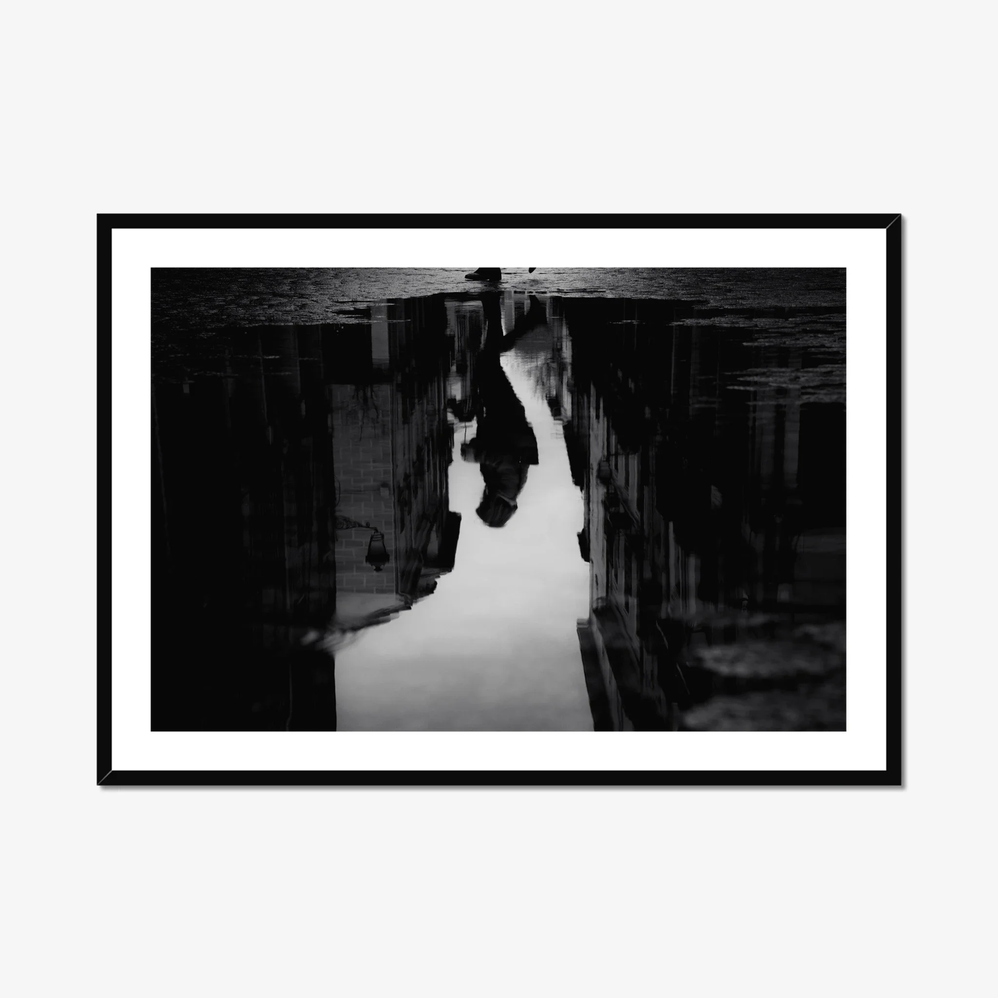 Black and white moody street photography print of a person with an umbrella walking in the rain. Features a striking reflection on wet pavement. Cinematic fine art wall decor.