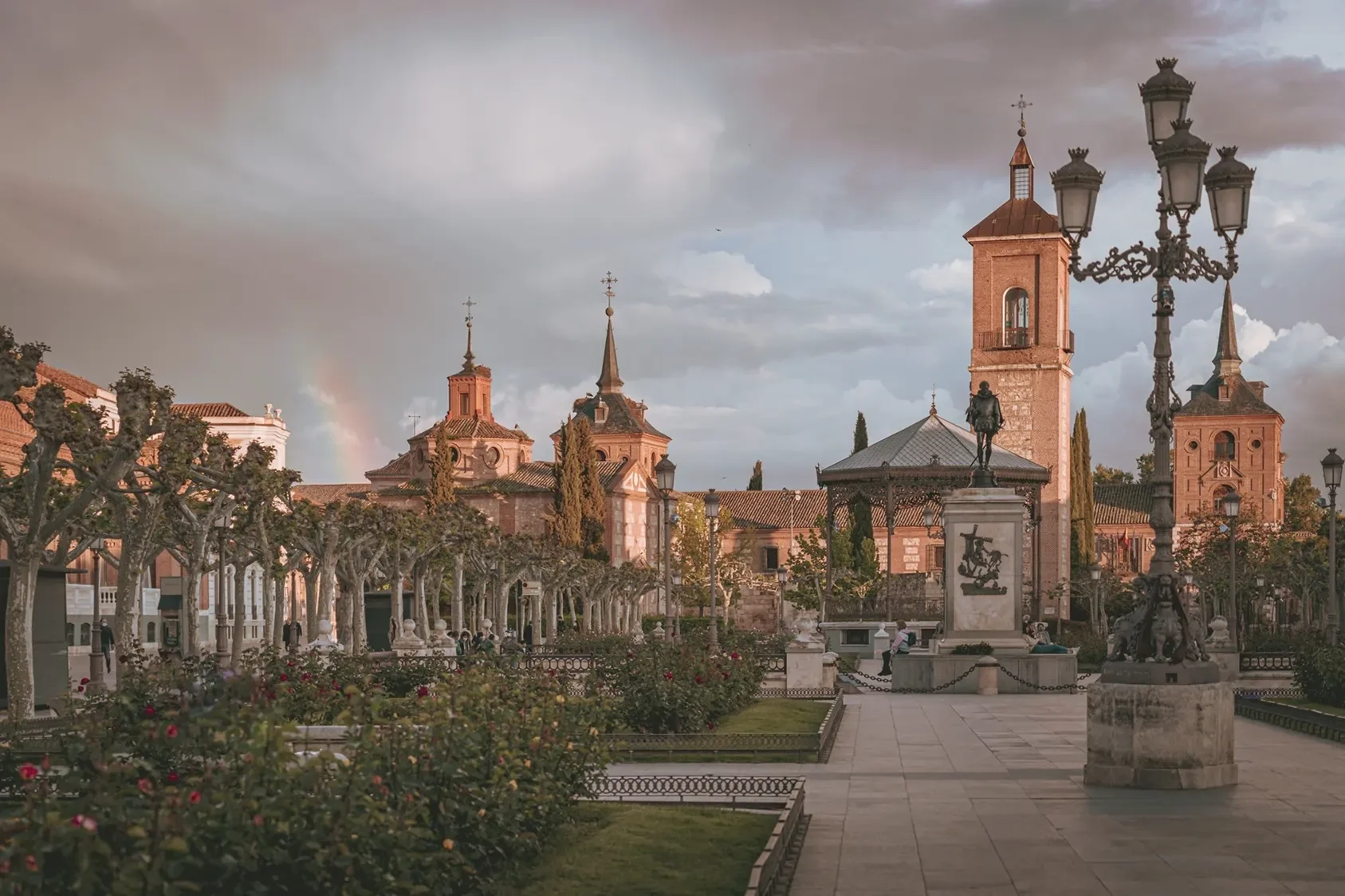 Fine art photography of Plaza de Cervantes in Alcala de Henares, Madrid, featuring a rainbow and dramatic stormy sunset over the historic square.