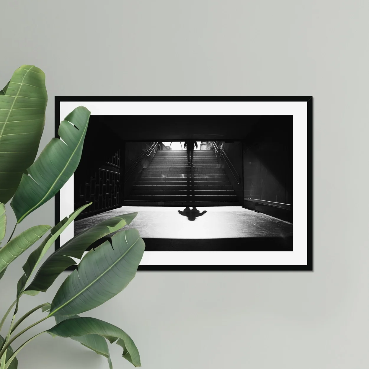 Black and white minimalist street photography of a person walking down stairs in Madrid Metro, casting a long diagonal shadow on a sunny morning.