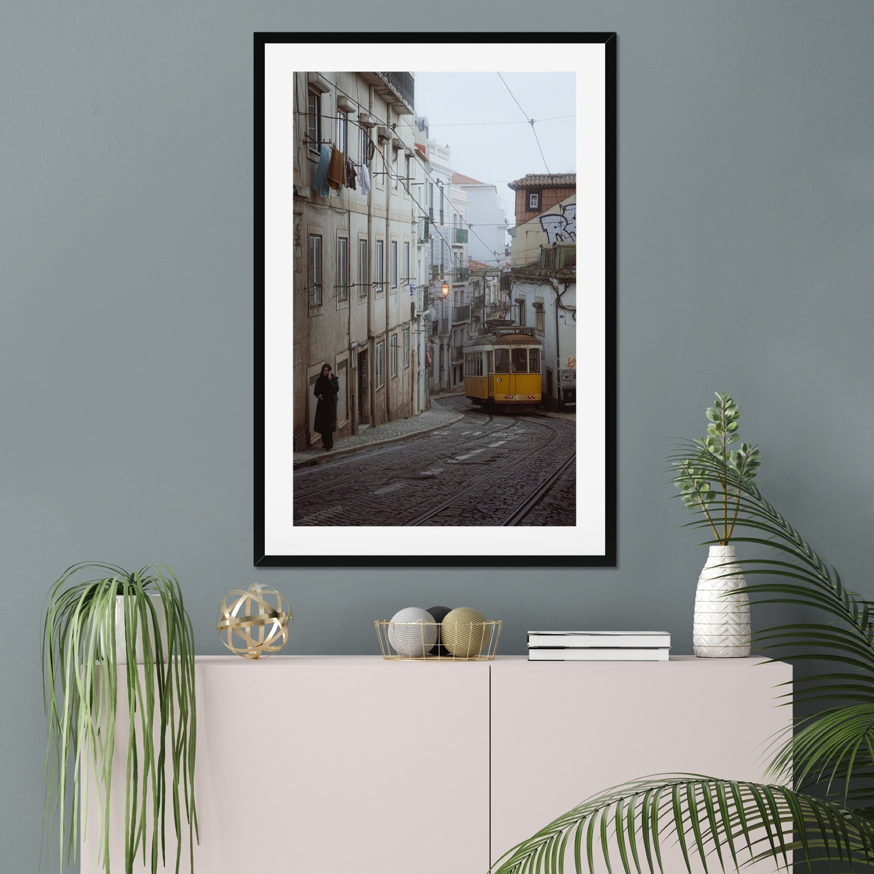 Black and white or muted tone photography of a Lisbon tram in Alfama street, winding cobblestone road with a person walking, minimalist Portuguese urban wall art.