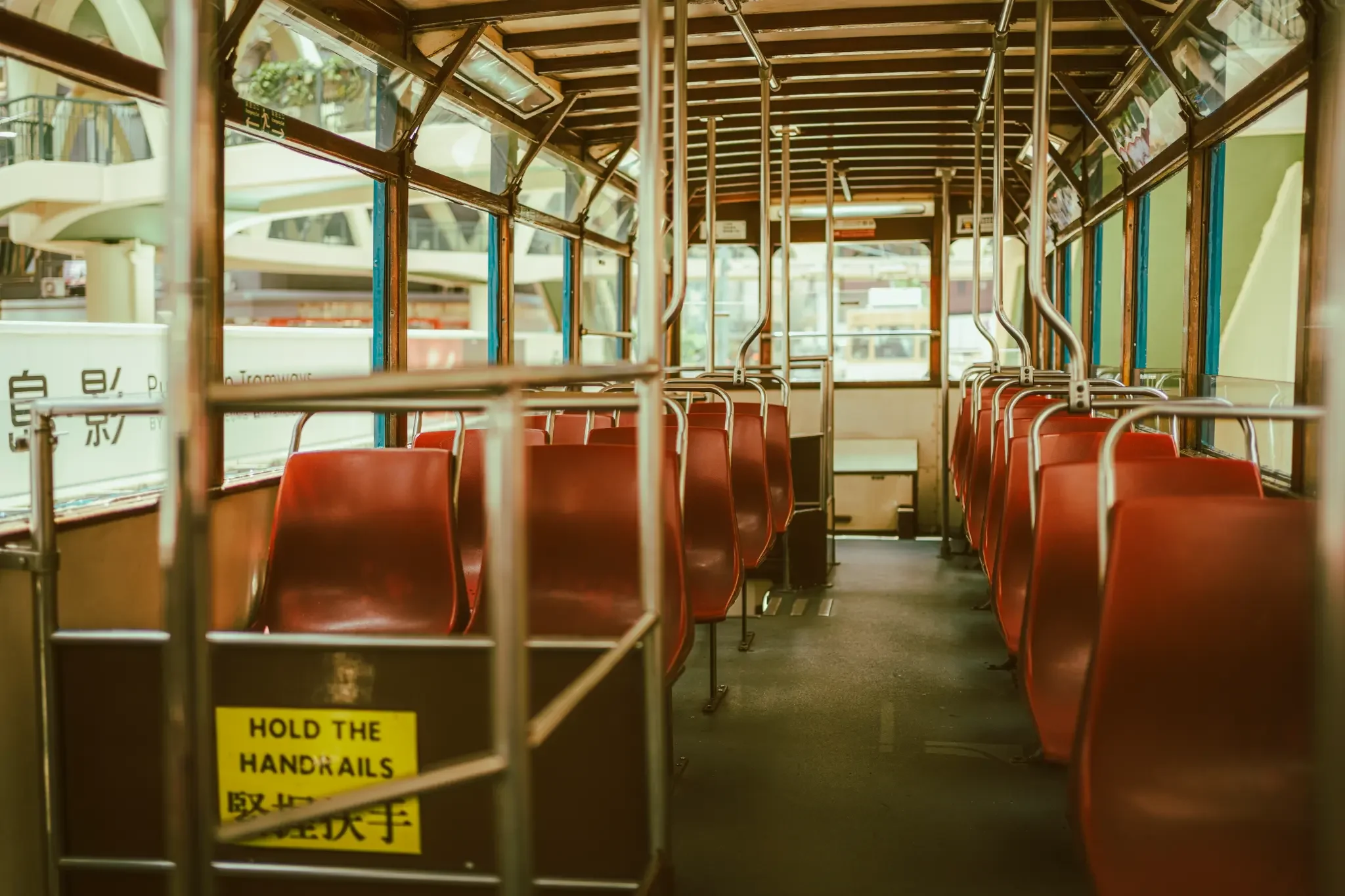 Vintage Hong Kong tram interior fine art print featuring red seats and a hold the handrails sign in warm cinematic tones.