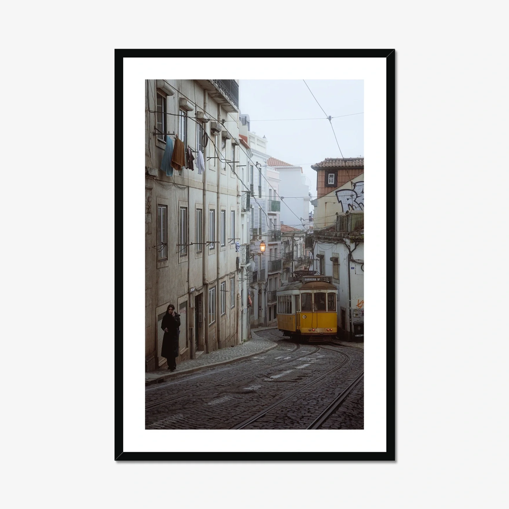 Black and white or muted tone photography of a Lisbon tram in Alfama street, winding cobblestone road with a person walking, minimalist Portuguese urban wall art.