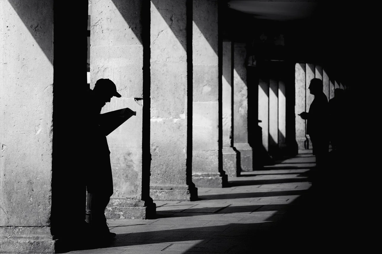 Black and white minimalist street photography print of a lone figure walking up an outdoor staircase. Features strong geometric lines and high-contrast dramatic shadows. Fine art wall decor.