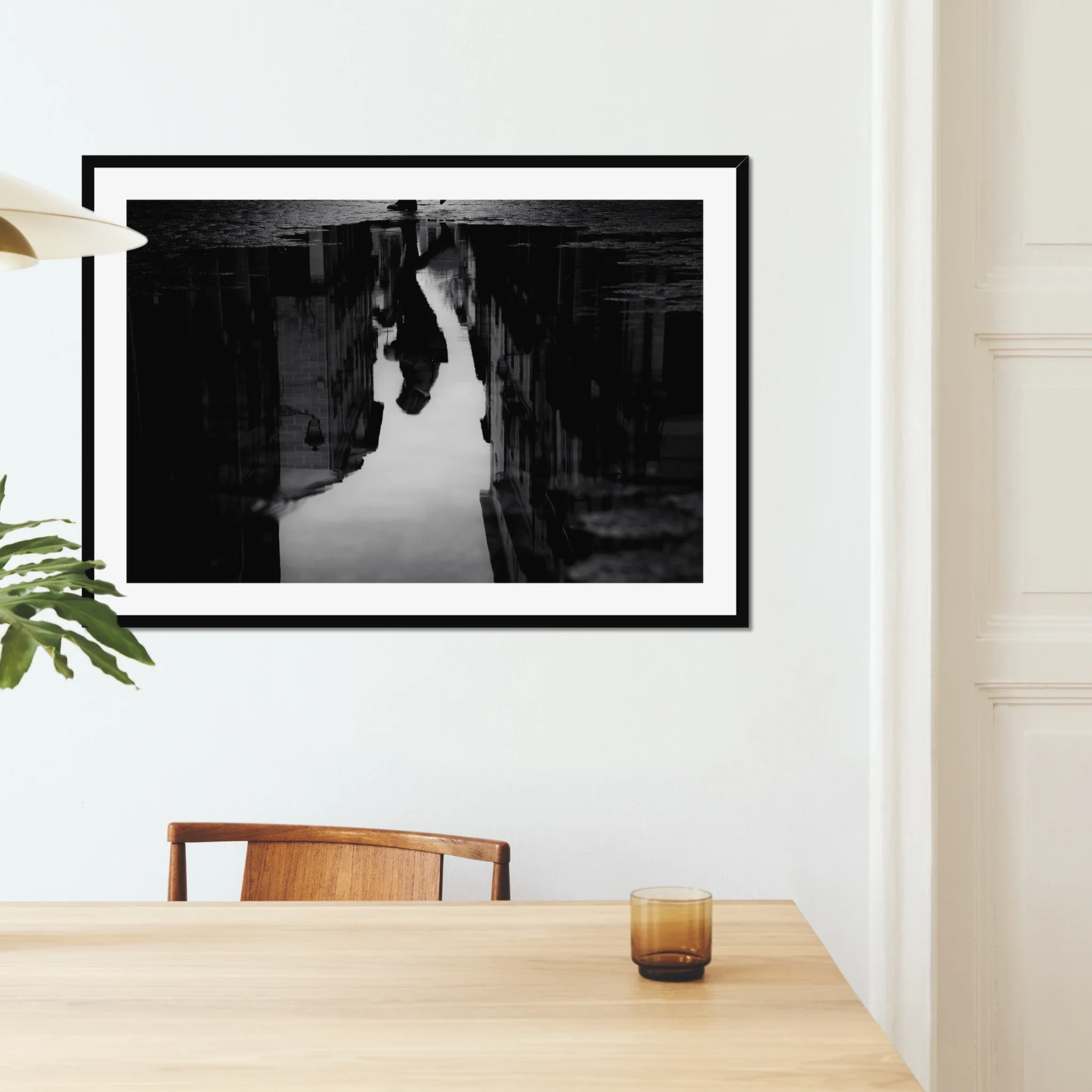 Black and white moody street photography print of a person with an umbrella walking in the rain. Features a striking reflection on wet pavement. Cinematic fine art wall decor.
