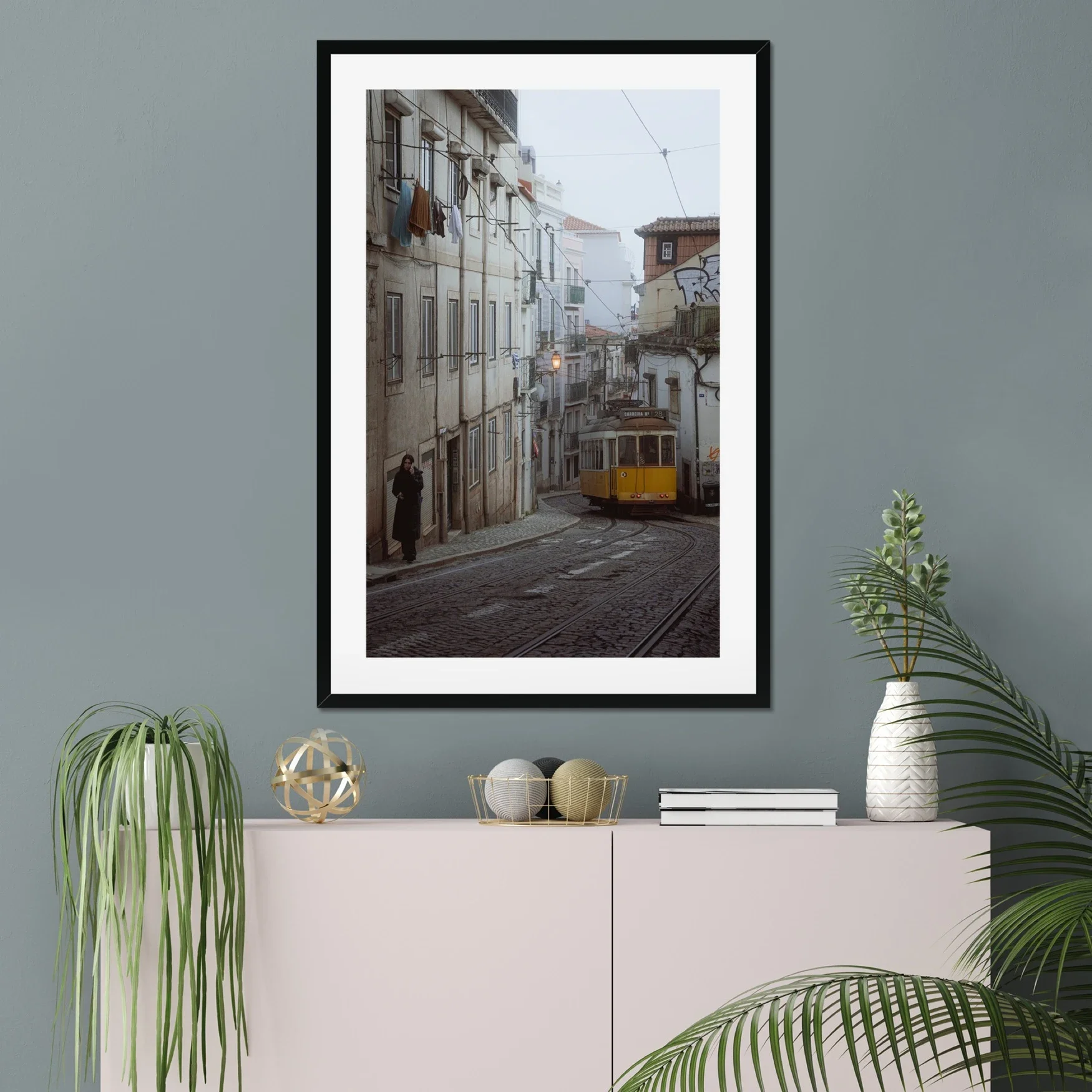 Black and white or muted tone photography of a Lisbon tram in Alfama street, winding cobblestone road with a person walking, minimalist Portuguese urban wall art.