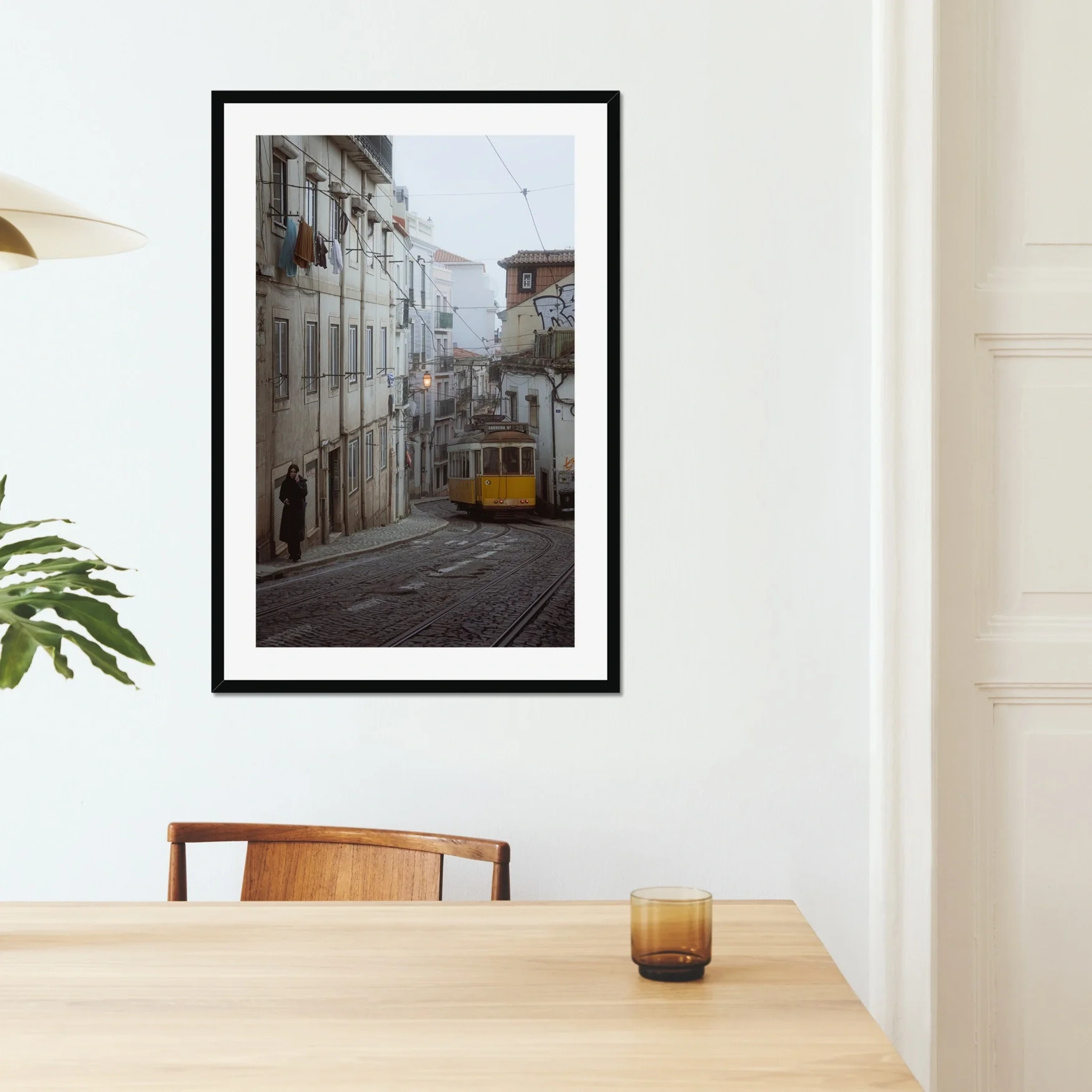 Black and white or muted tone photography of a Lisbon tram in Alfama street, winding cobblestone road with a person walking, minimalist Portuguese urban wall art.