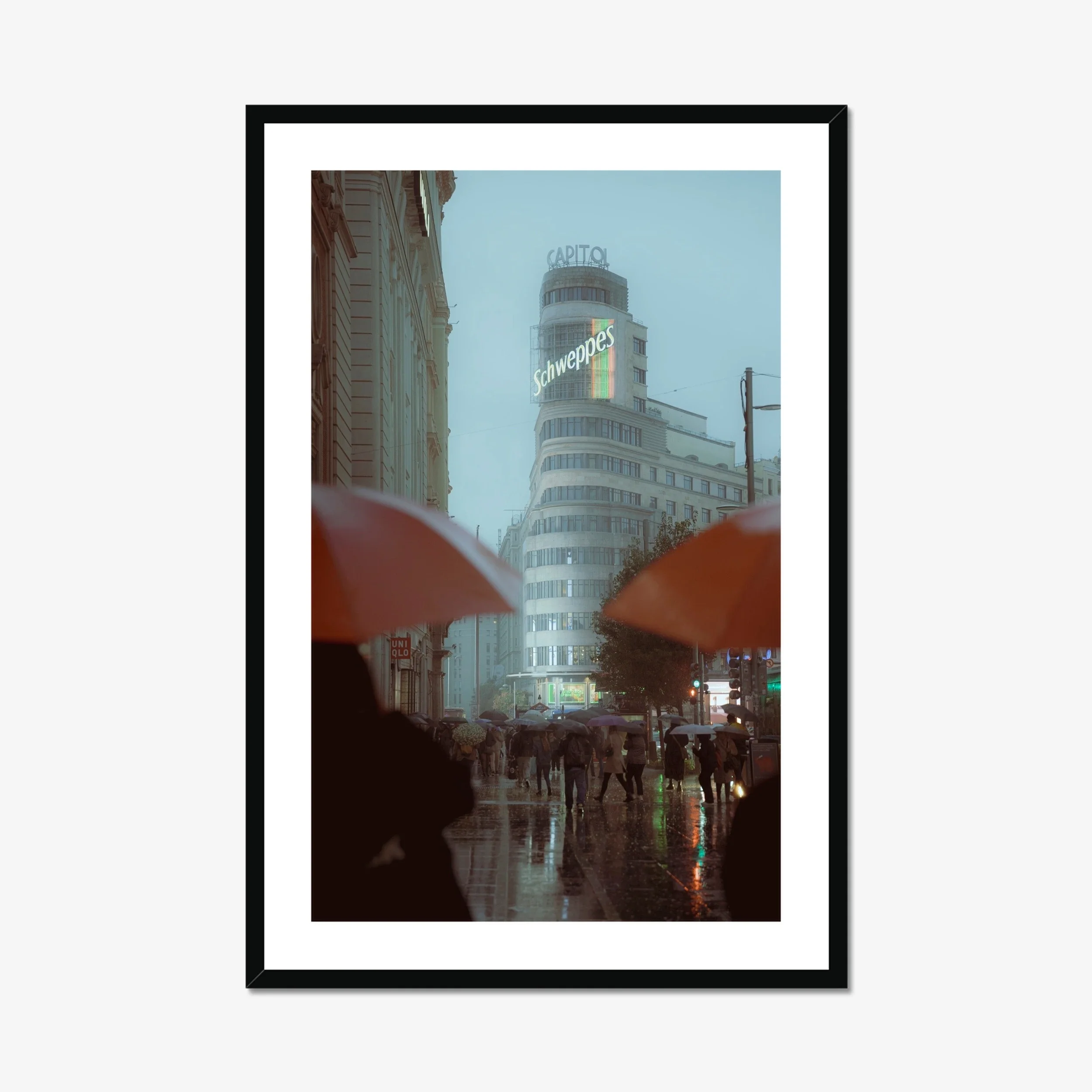 Cinematic street photography of Gran Via Madrid in the rain, featuring the Schweppes Capitol building, a sea of umbrellas, and wet street reflections at dusk.