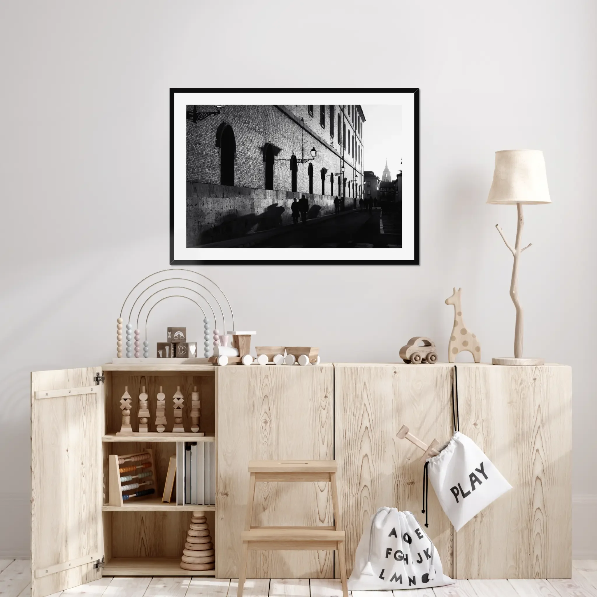 Black and white street photography print of a person walking past a textured historical wall. Features striking diagonal shadows and high-contrast lighting. Classic fine art monochrome decor.