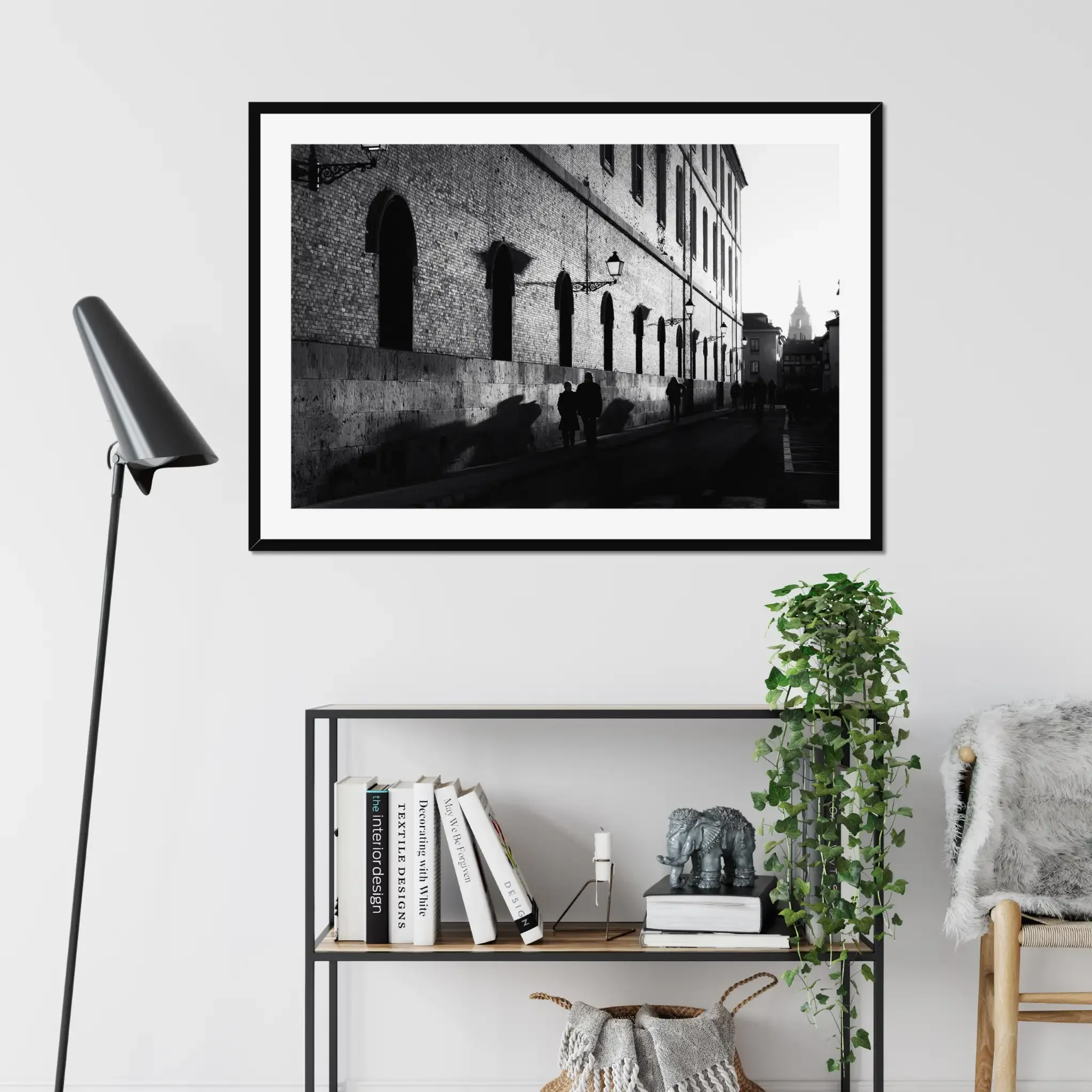 Black and white street photography print of a person walking past a textured historical wall. Features striking diagonal shadows and high-contrast lighting. Classic fine art monochrome decor.