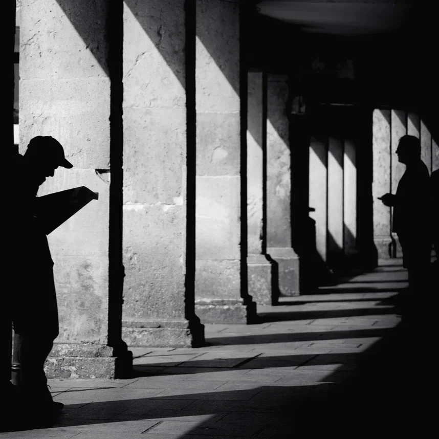 High contrast black and white photography of a figure in shadows under arches.