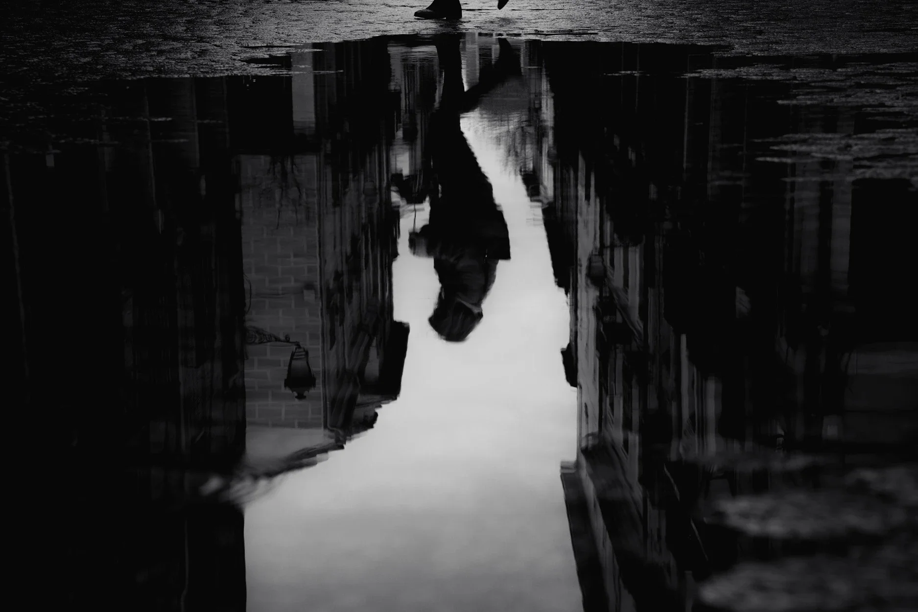 Black and white moody street photography print of a person with an umbrella walking in the rain. Features a striking reflection on wet pavement. Cinematic fine art wall decor.