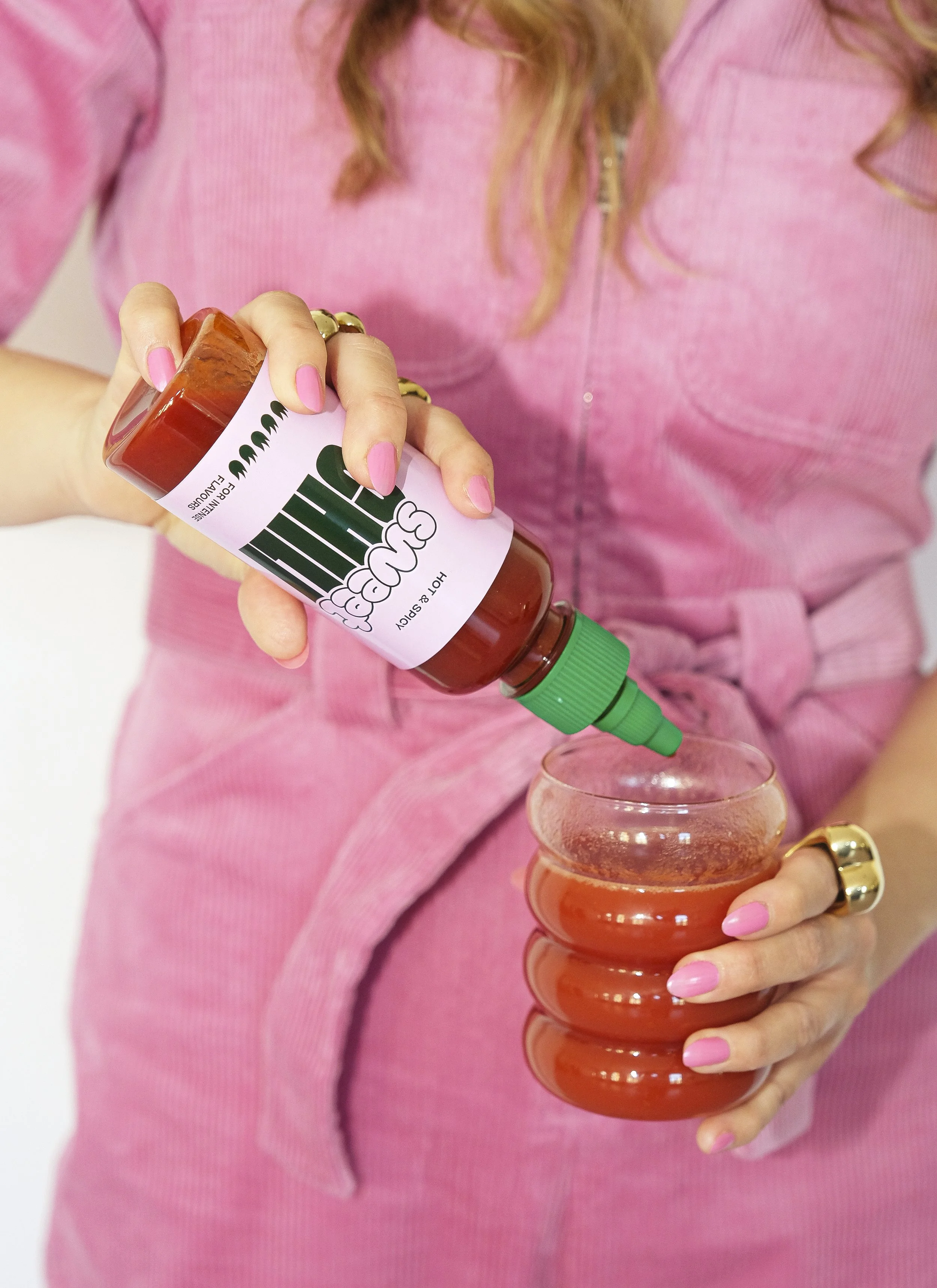 Eine Person in einem pinken Kleid gießt scharfe Soße aus einer Flasche in einu glas