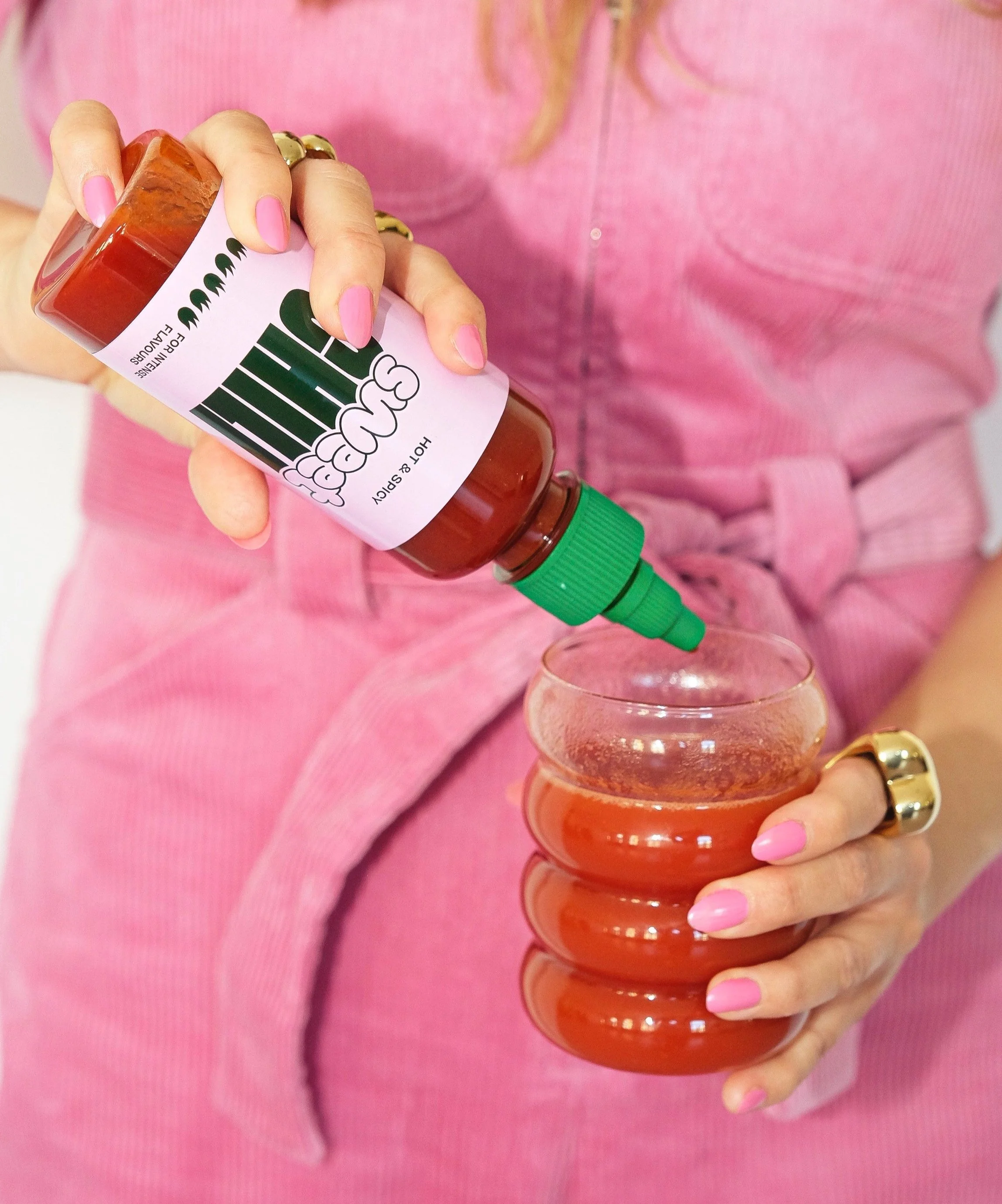 Eine Person im pinken Outfit gießt eine rote Soße aus einer Flasche in ein Glas