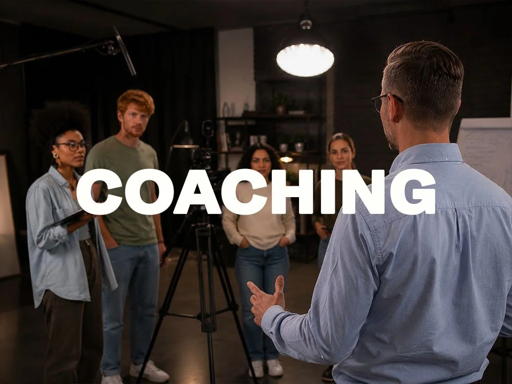 Ein Mann in einem blauen Hemd gibt Coaching an eine Gruppe von vier jungen Erwachsenen in einem Studio oder Konferenzraum, mit Kamera und Beleuchtung. Der Begriff "COACHING" ist groß in der Mitte sichtbar.