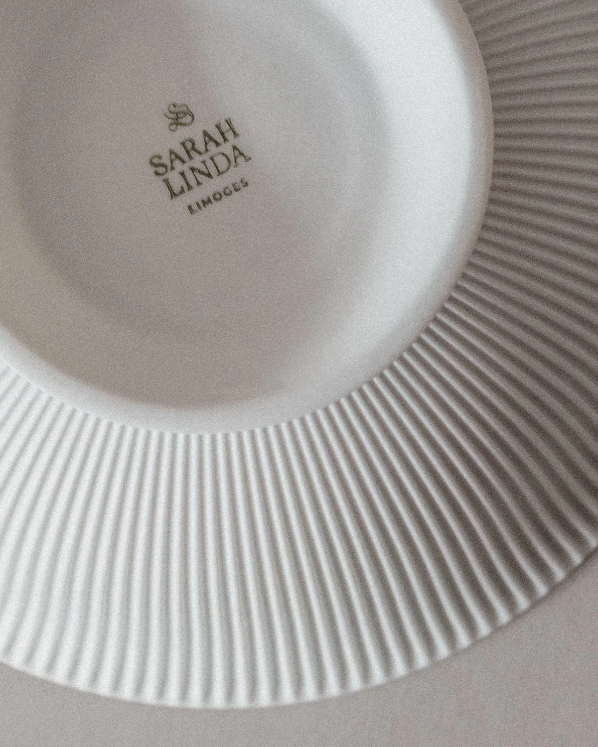 Close-up of a white Eros ceramic plate stamped Sarah Linda, Limoges, Sensual tableware, branding, web design and editorial project by Automne Studio.