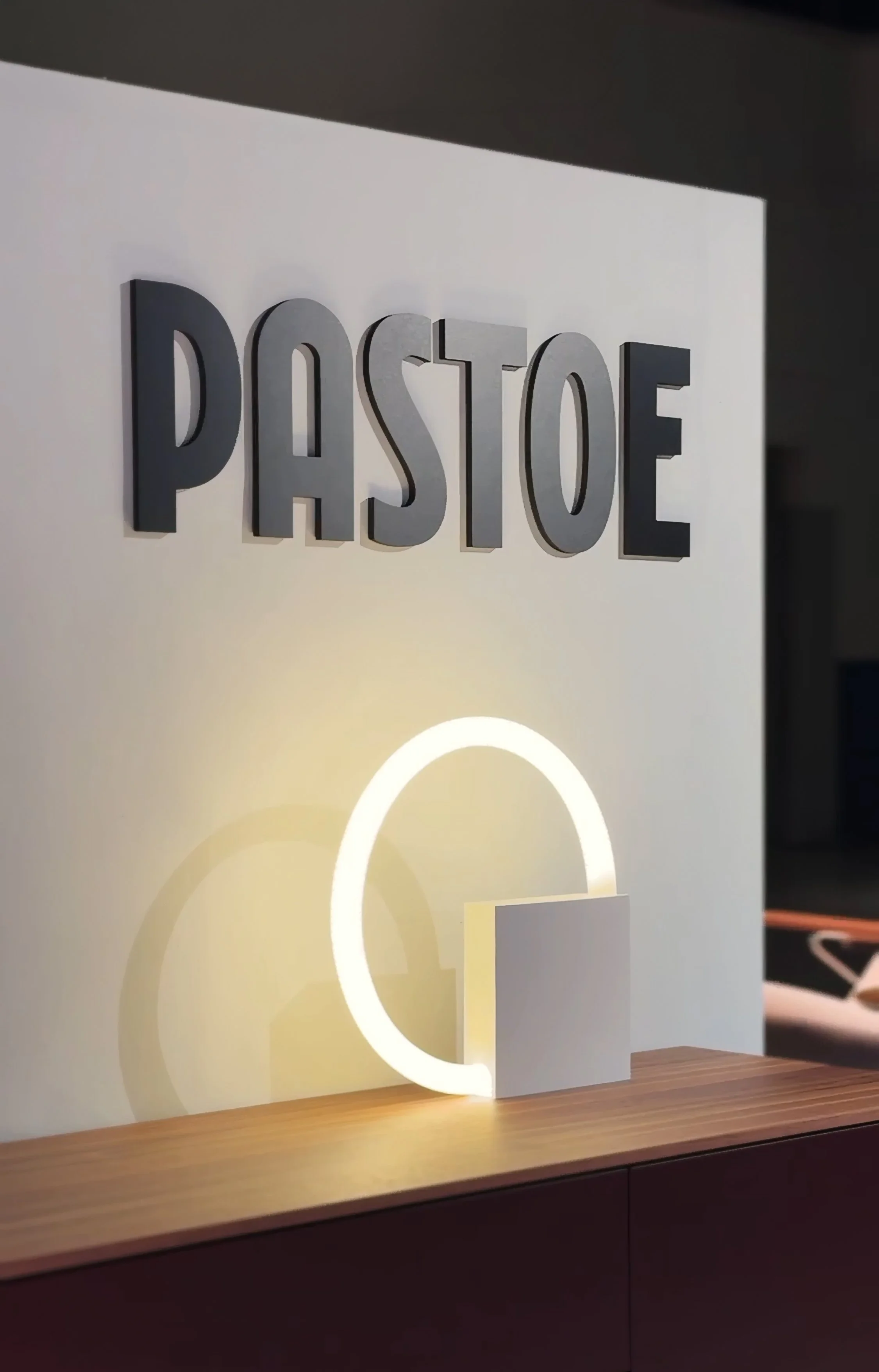 Close-up of a stylish home bar with raised “PASTOE” lettering and a glowing circular light, timeless dutch furniture design, branding and illustration project by Automne Studio.