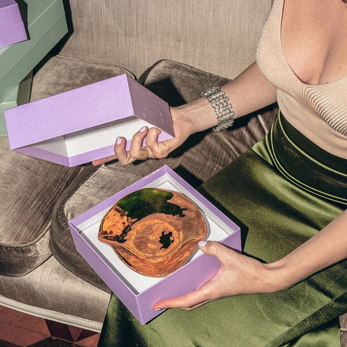 Woman in a green satin skirt unpacking a purple Sarah-Linda tableware box, sensual tableware, branding, web design and editorial project by Automne Studio.