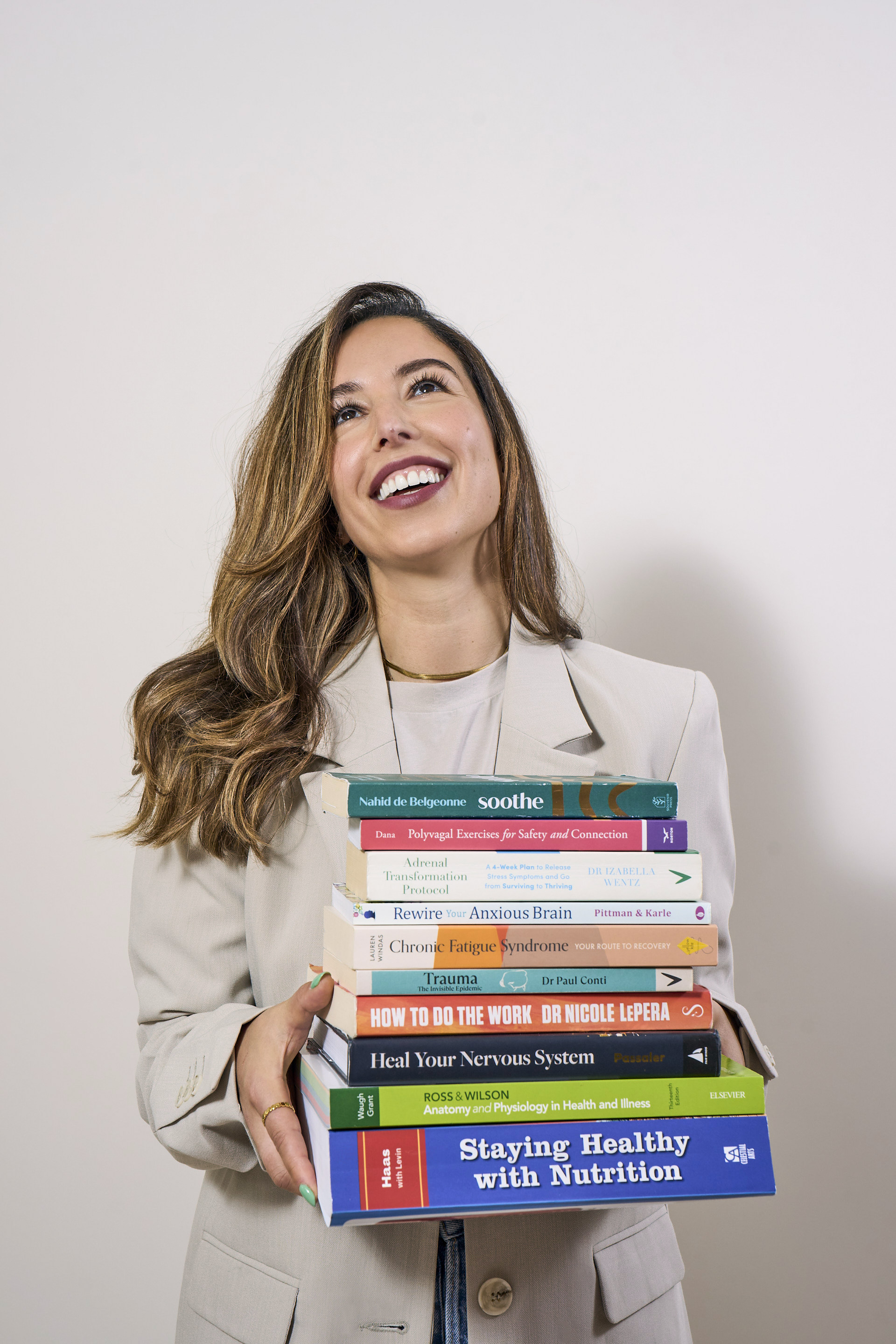 A woman smiling and looking up while holding a stack of health and wellness books.