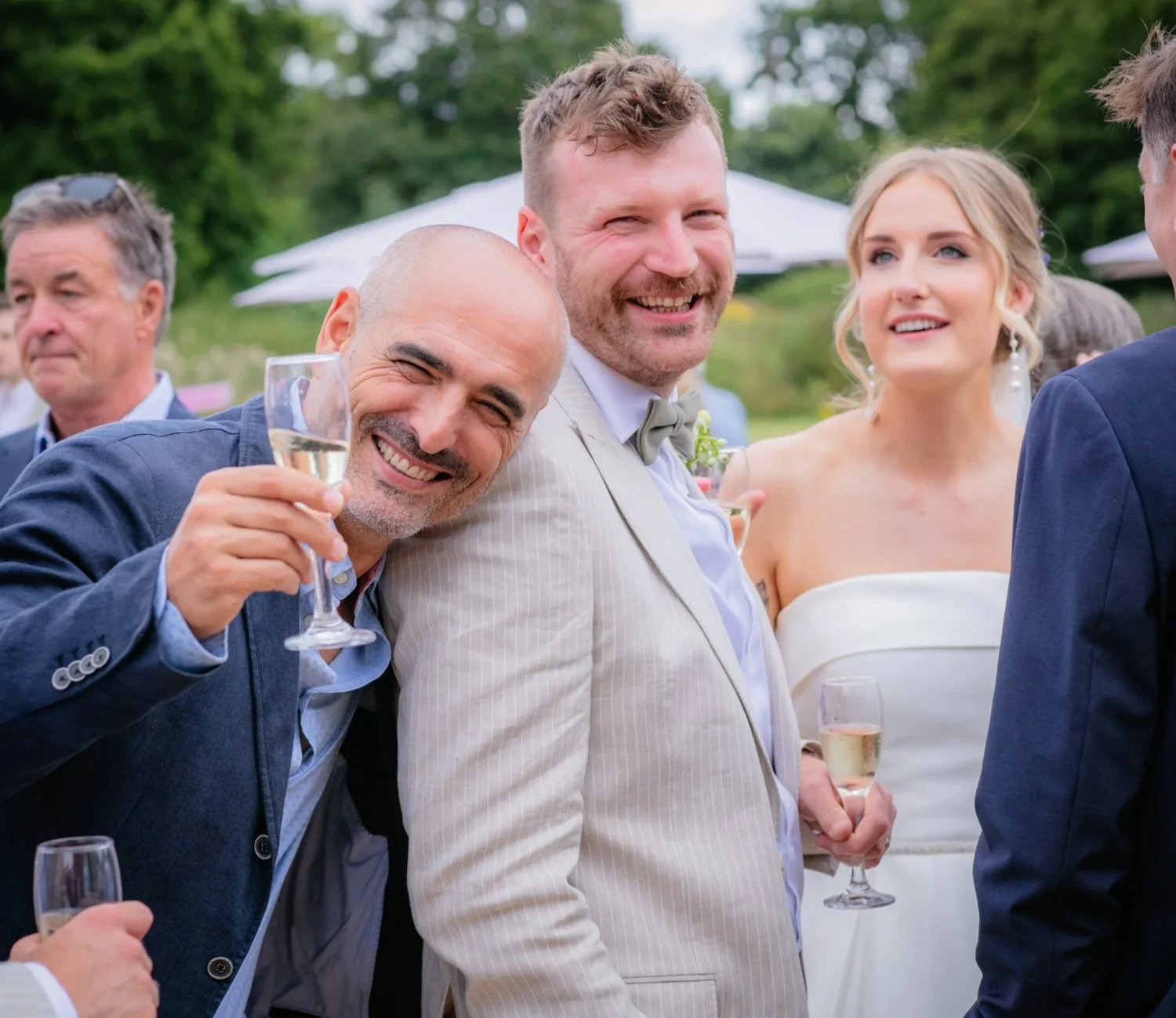 People celebrating at an outdoor wedding reception, smiling and holding champagne glasses.