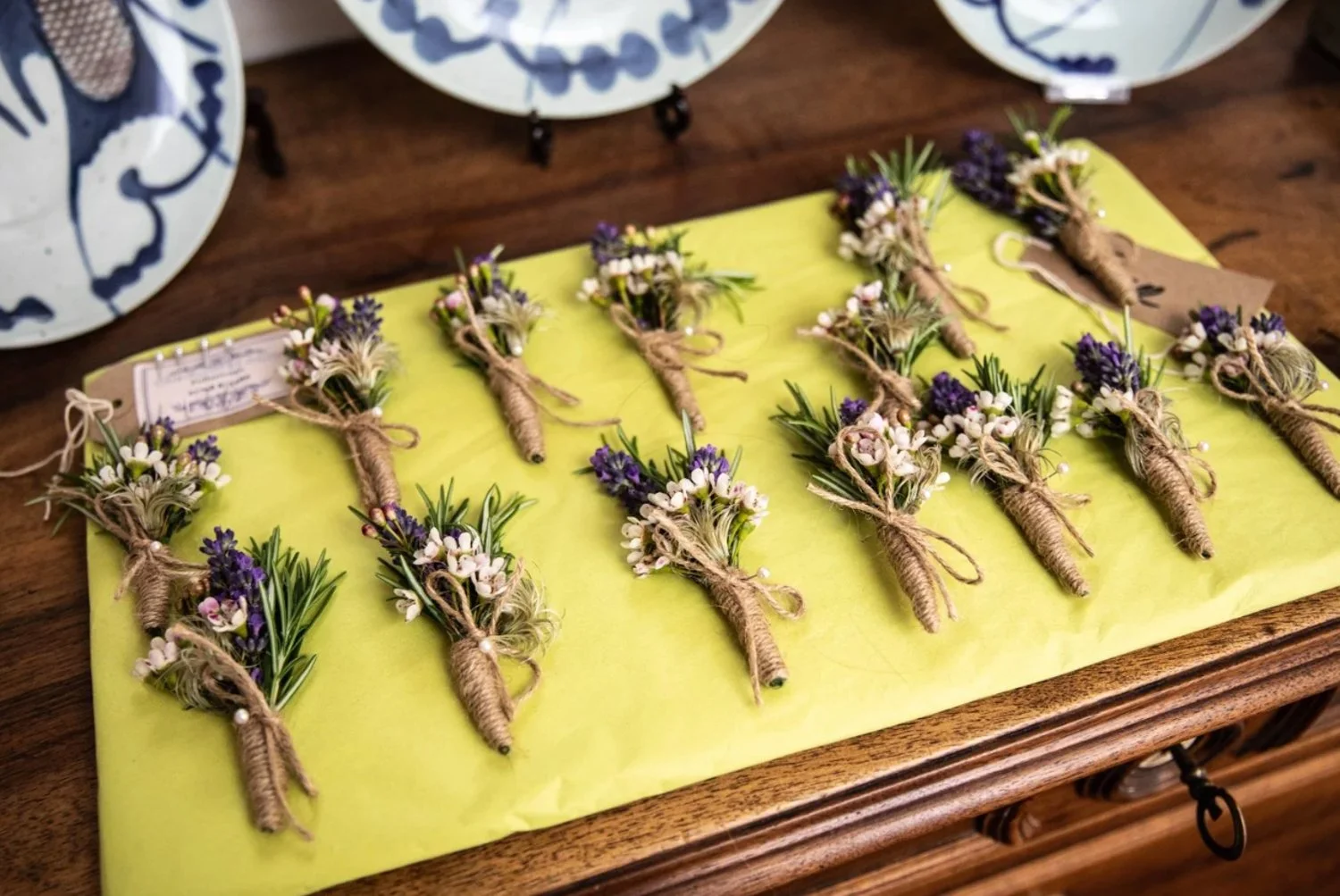 Small handcrafted lavender and white flower boutonnières wrapped in twine, arranged on a yellow surface.