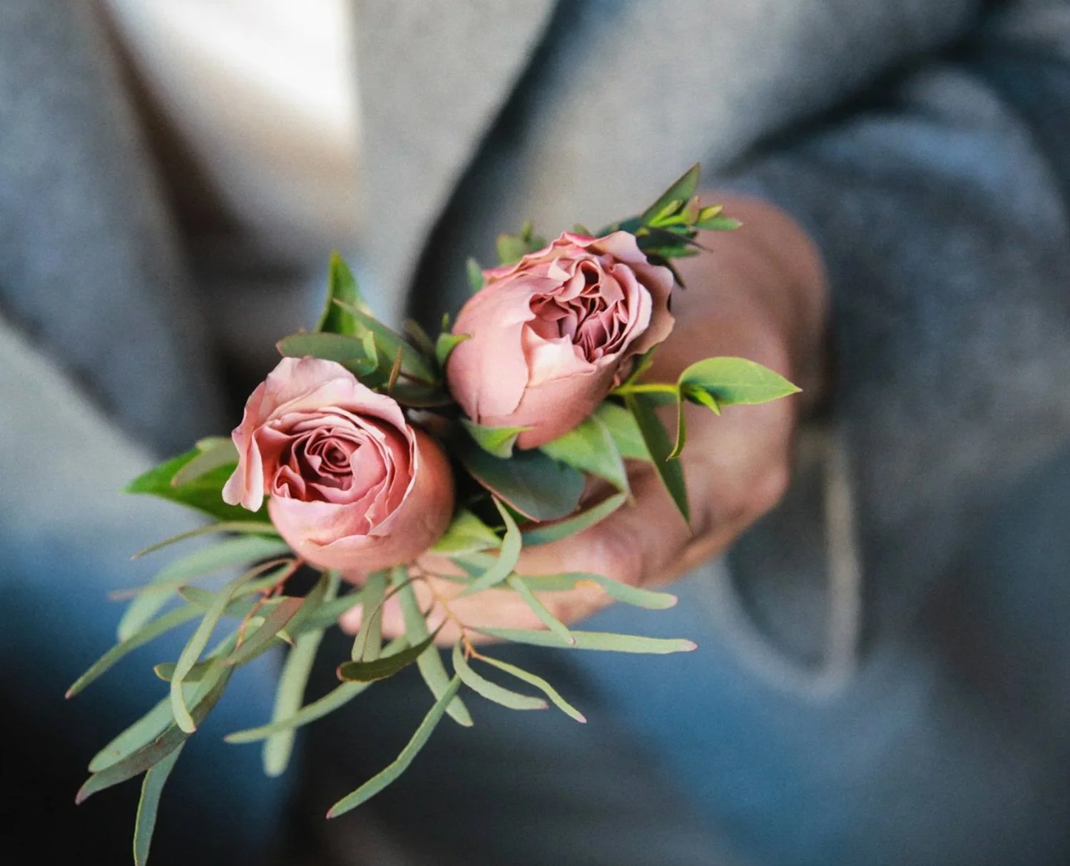 Person holding a small bouquet of pink roses with green leaves.