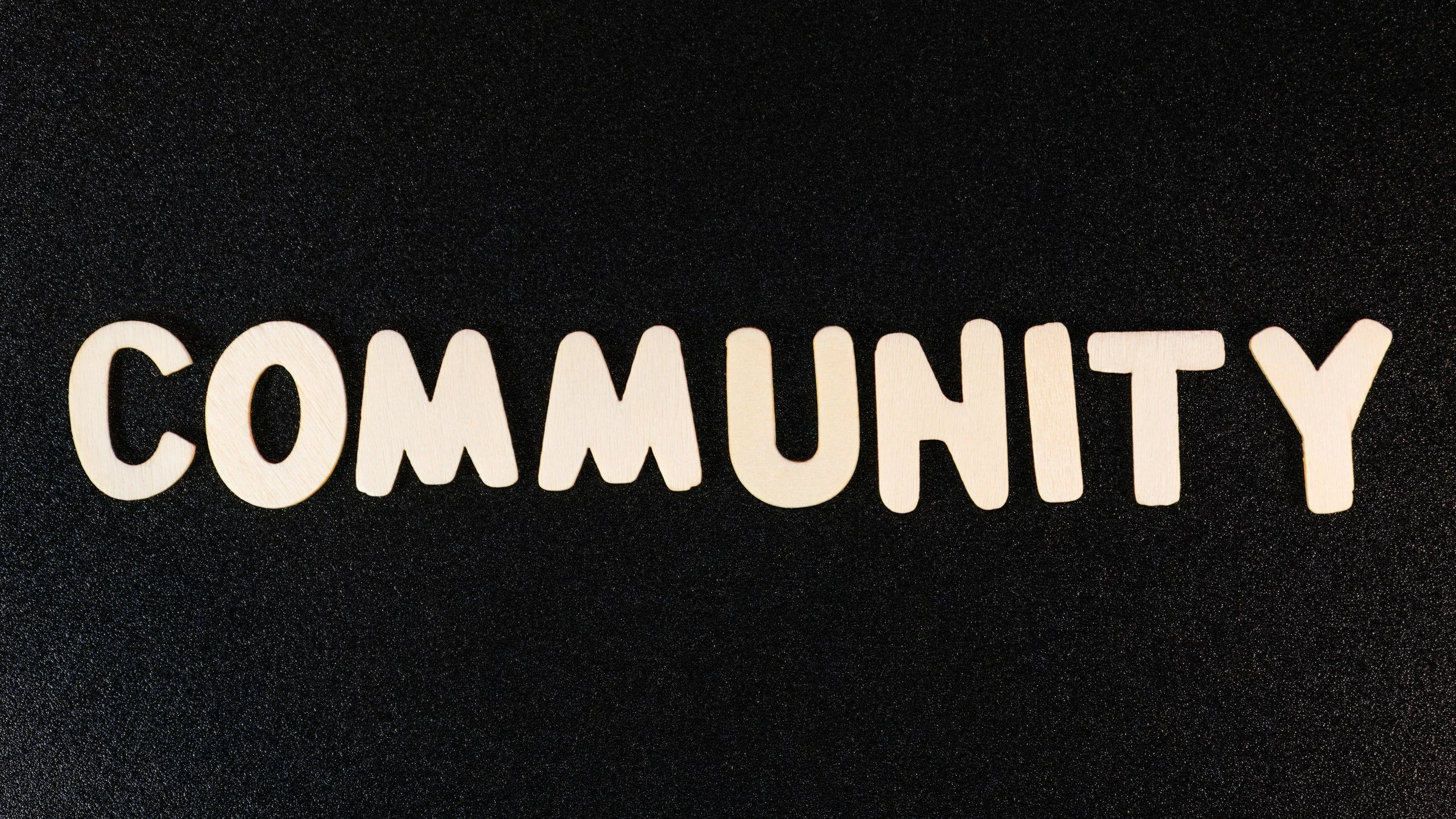 Wooden letters spelling out 'Community' on a black textured background.