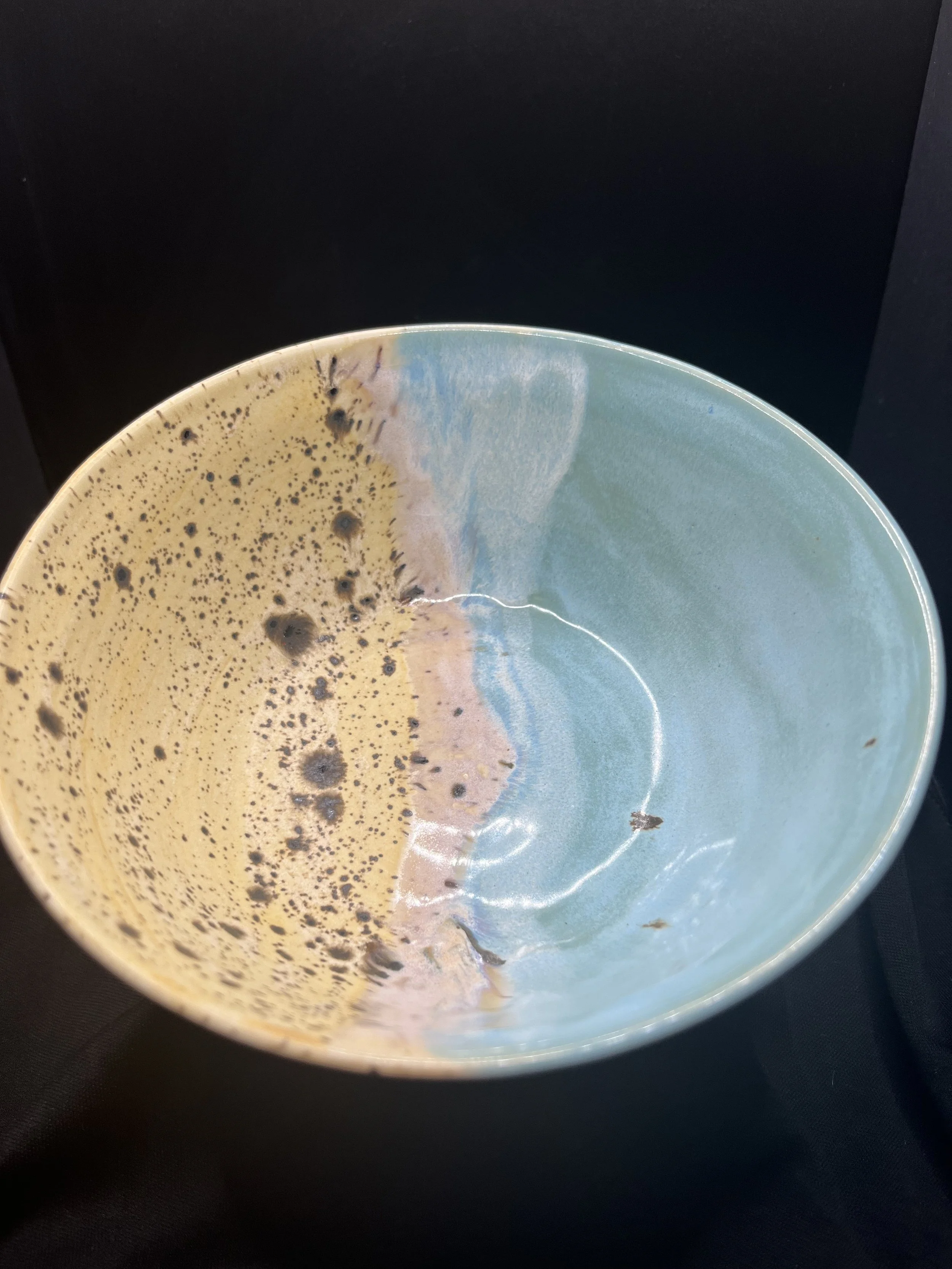 A ceramic bowl with a colorful glaze of yellow, blue, and pink, containing dark coffee grounds or remnants. The bowl is set against a dark background.