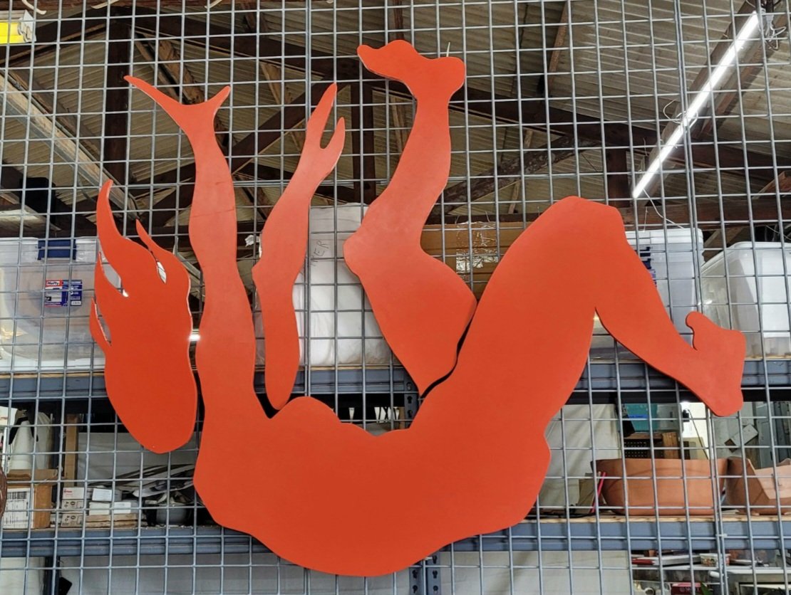 Orange silhouette of a woman in a yoga pose, hanging upside down with arms and legs extended.