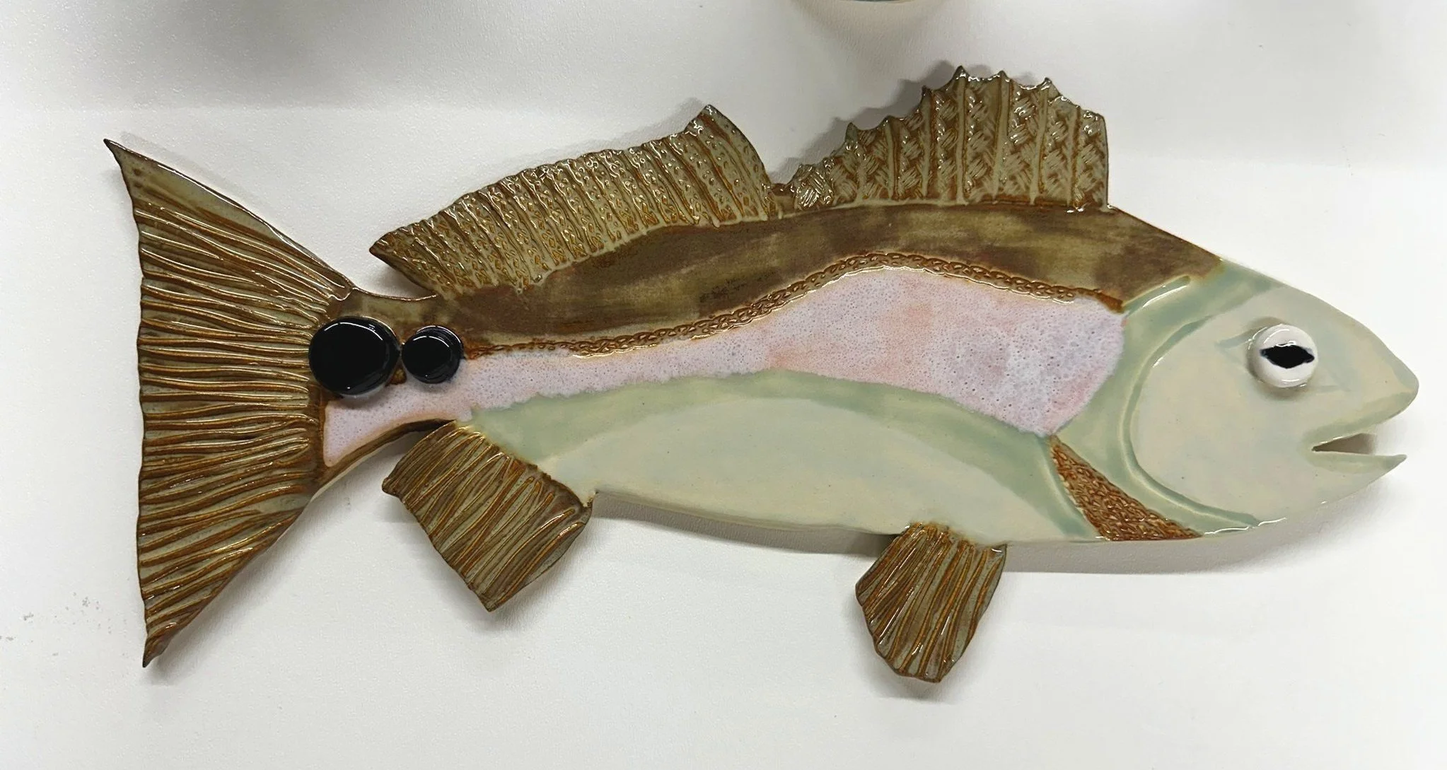 Lizette Terral Pottery Artist Decorative fish-shaped wall sculpture with golden fins and a multicolored body featuring pink, green, and gold accents, accented with black and white circular eyes.