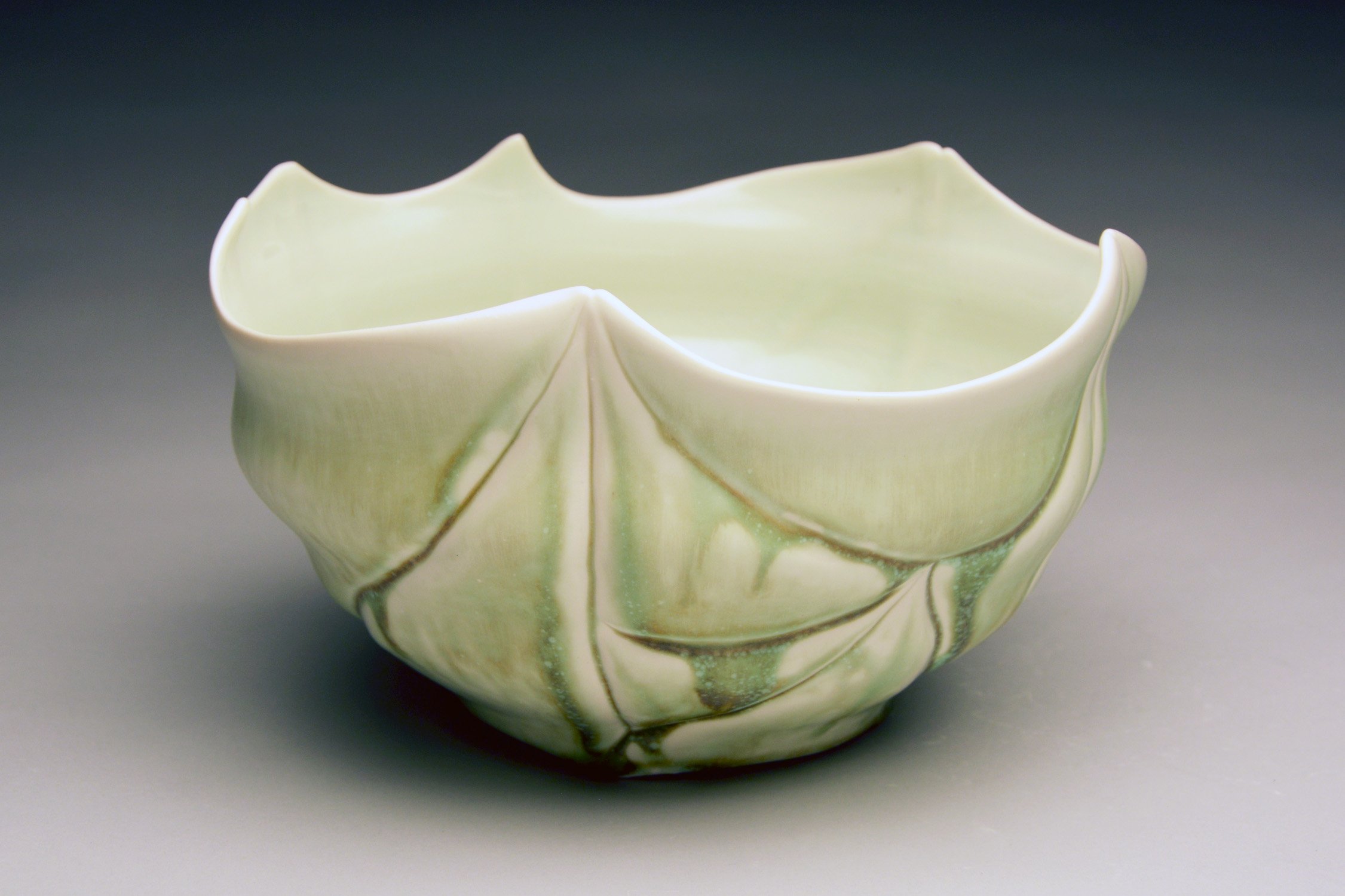 A ceramic bowl with a leaf design in shades of green and cream with a wavy, scalloped rim.