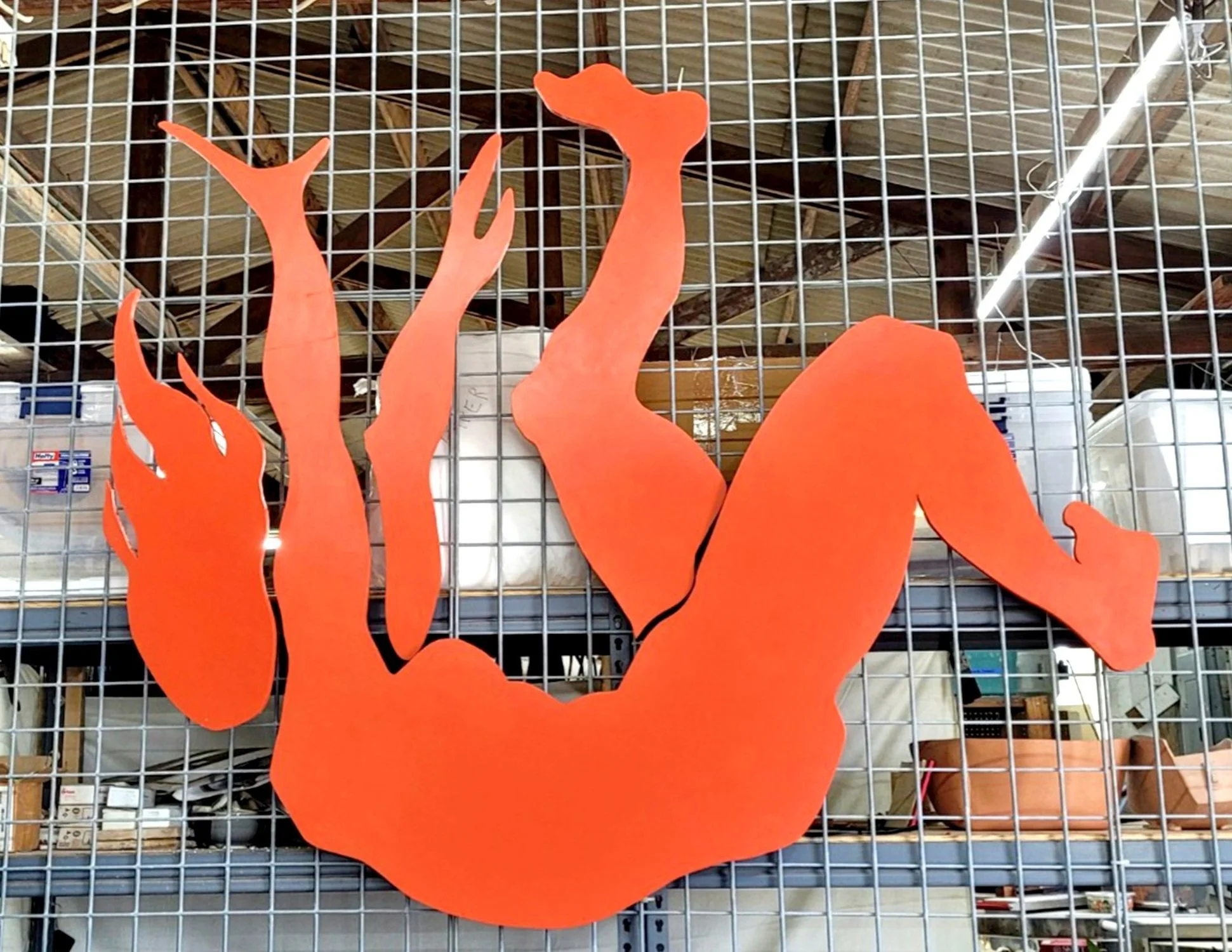 A red silhouette of a reclining woman with one arm raised and the other behind her head, displayed on a metal grid.